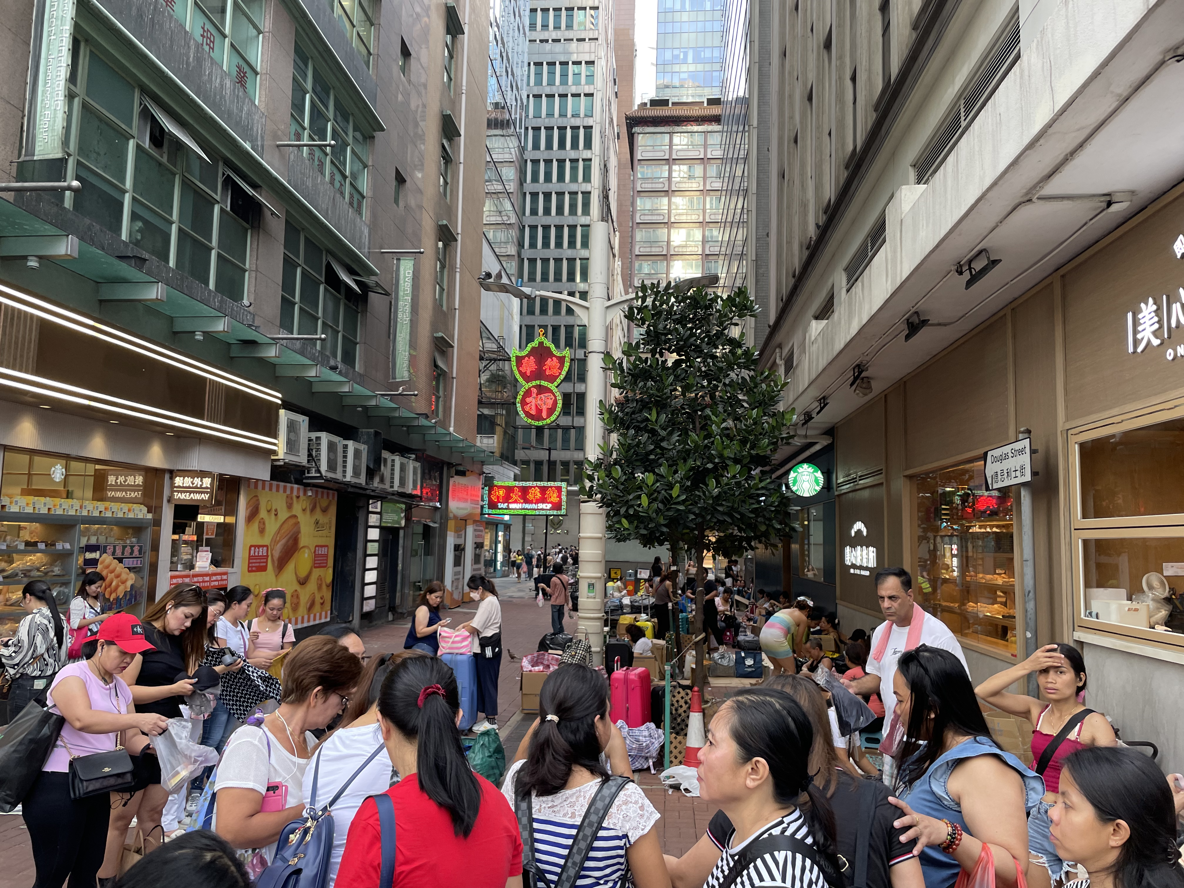 Women gathered on a pedestrianised street in the Central District of Hong Kong. There are high rise buildings on either side.