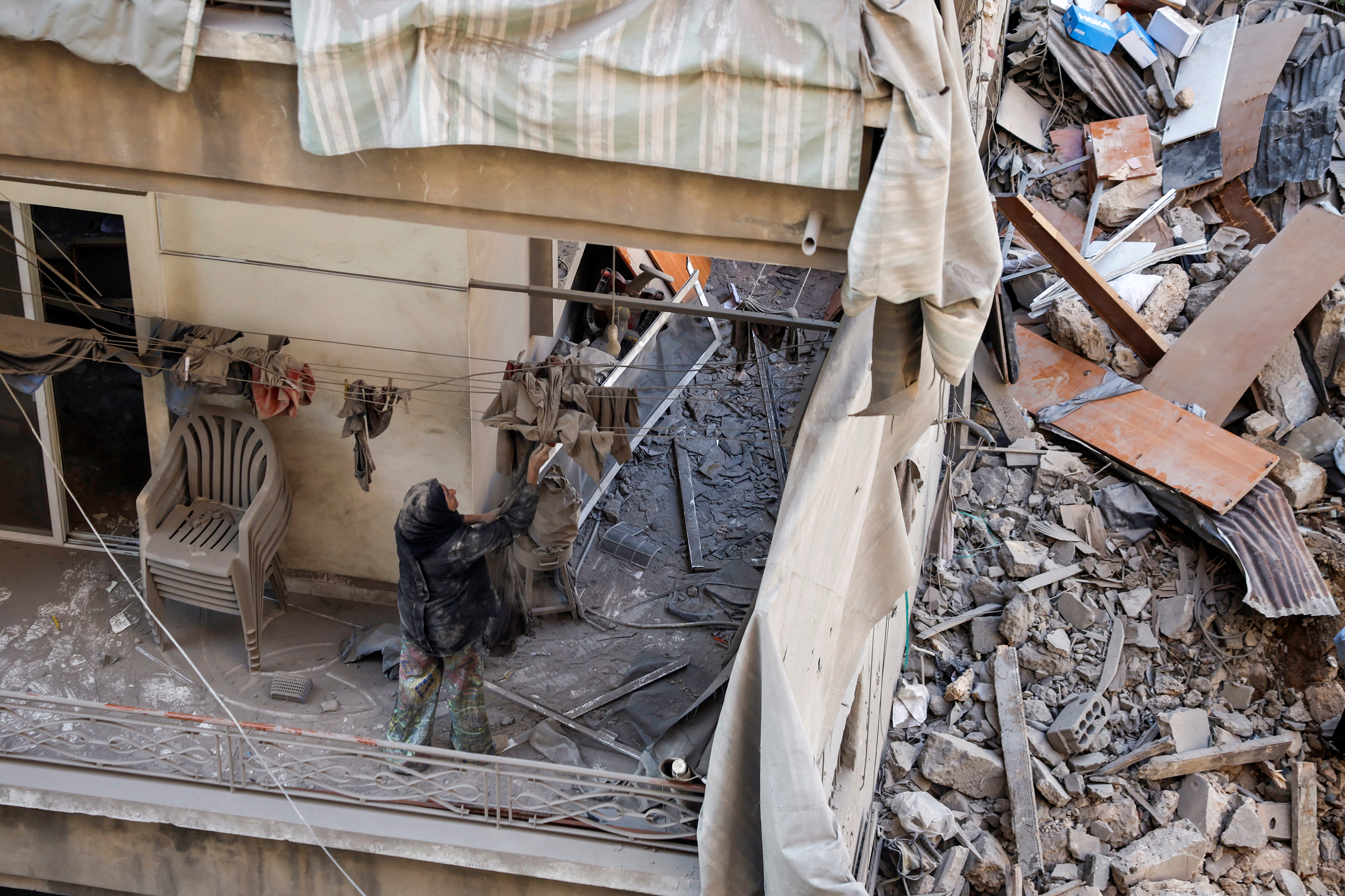 Maha Haddad, mother-in-law of Ahmed Al-Khatib cleans rubble in their damaged apartment at the strike site in Beirut, Lebanon, October 11