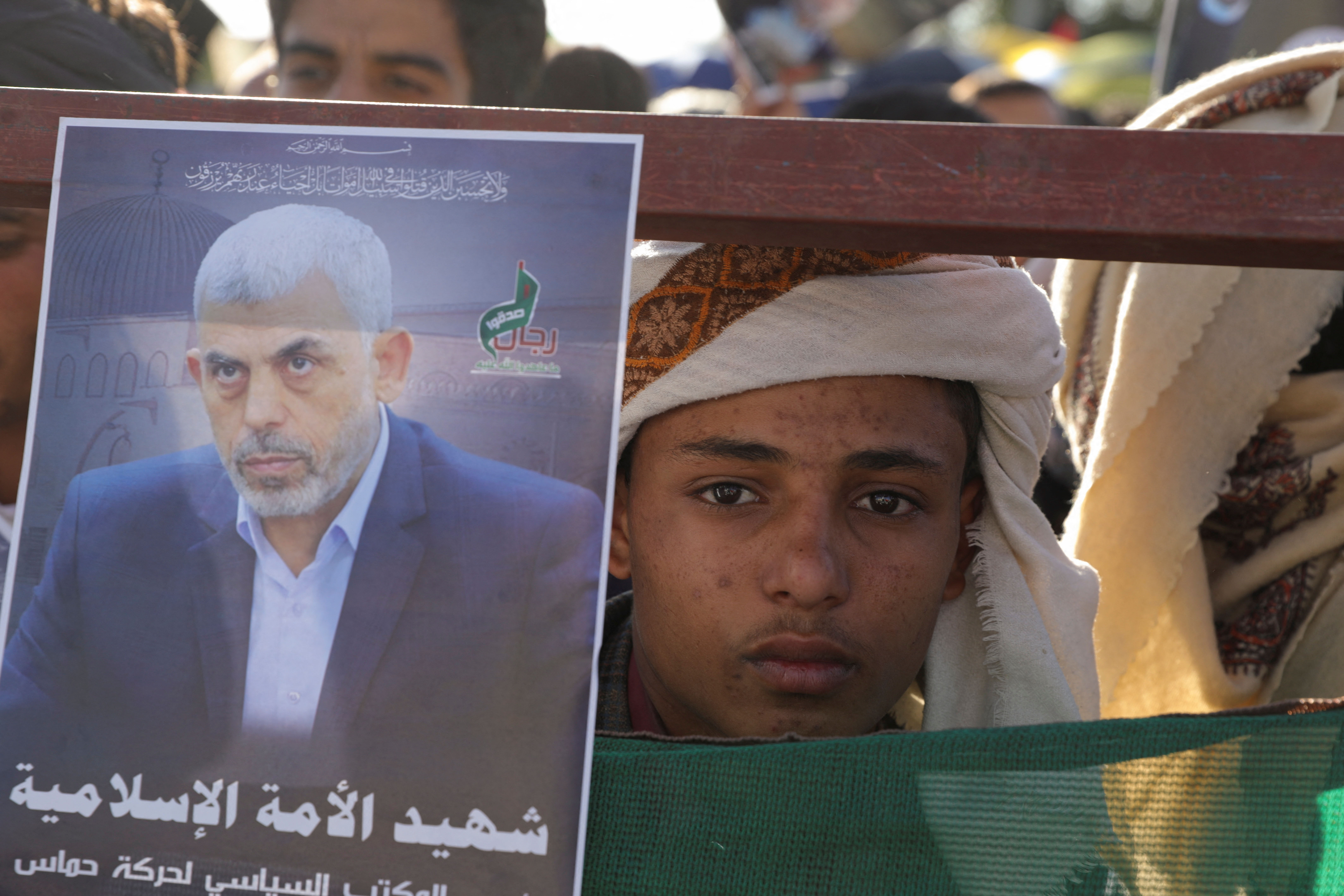 A person looks from behind a portrait of the late Hamas leader Yahya Sinwar, on a barricade at the site of a rally by protesters, mainly Houthi supporters, to show support to Lebanon's Hezbollah and Palestinians in the Gaza Strip, in Sanaa, Yemen October 18, 2024. REUTERS/Khaled Abdullah