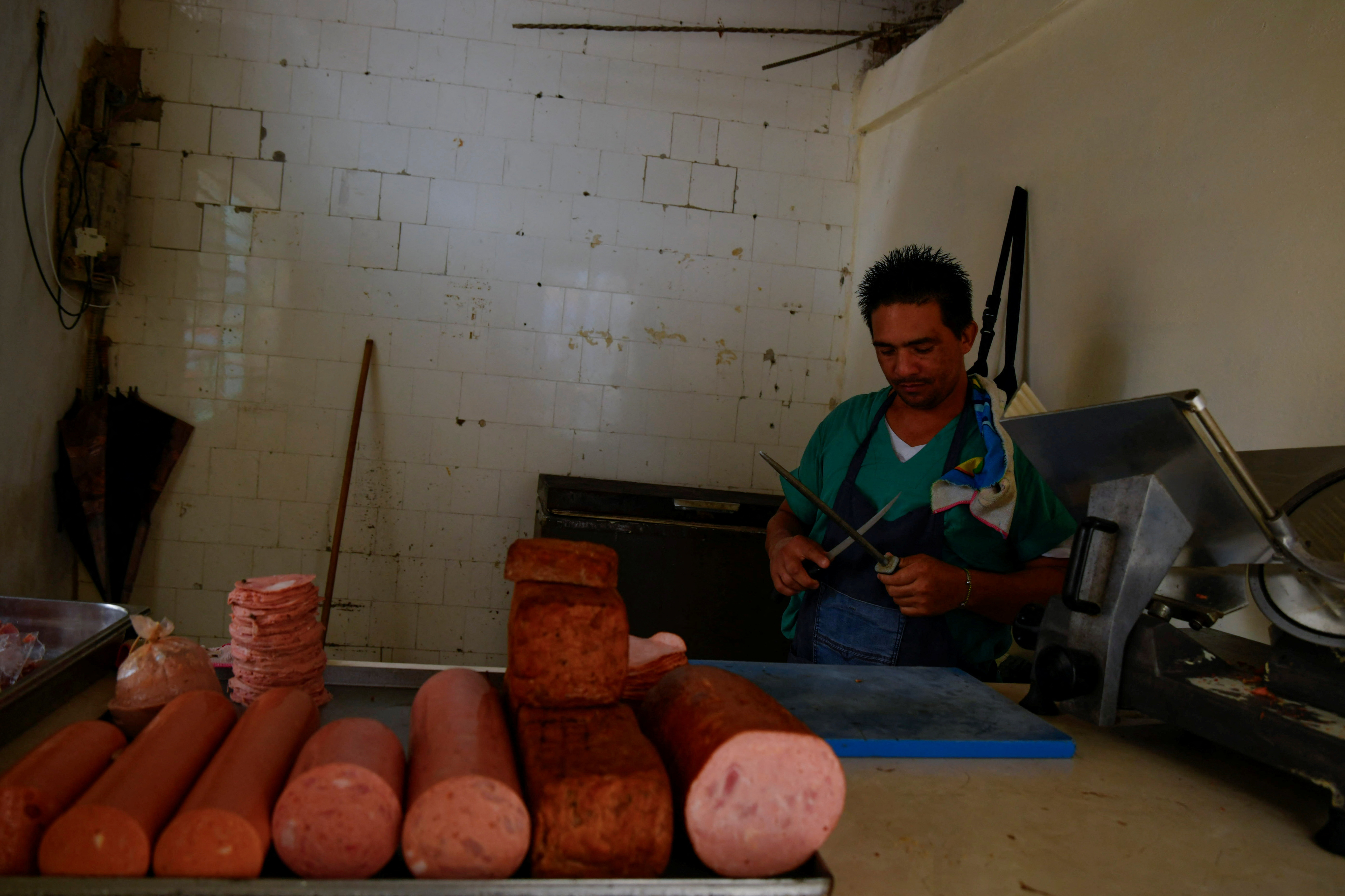 A butcher sits behind a meat counter, where rolls of deli meat sit during a blackout.