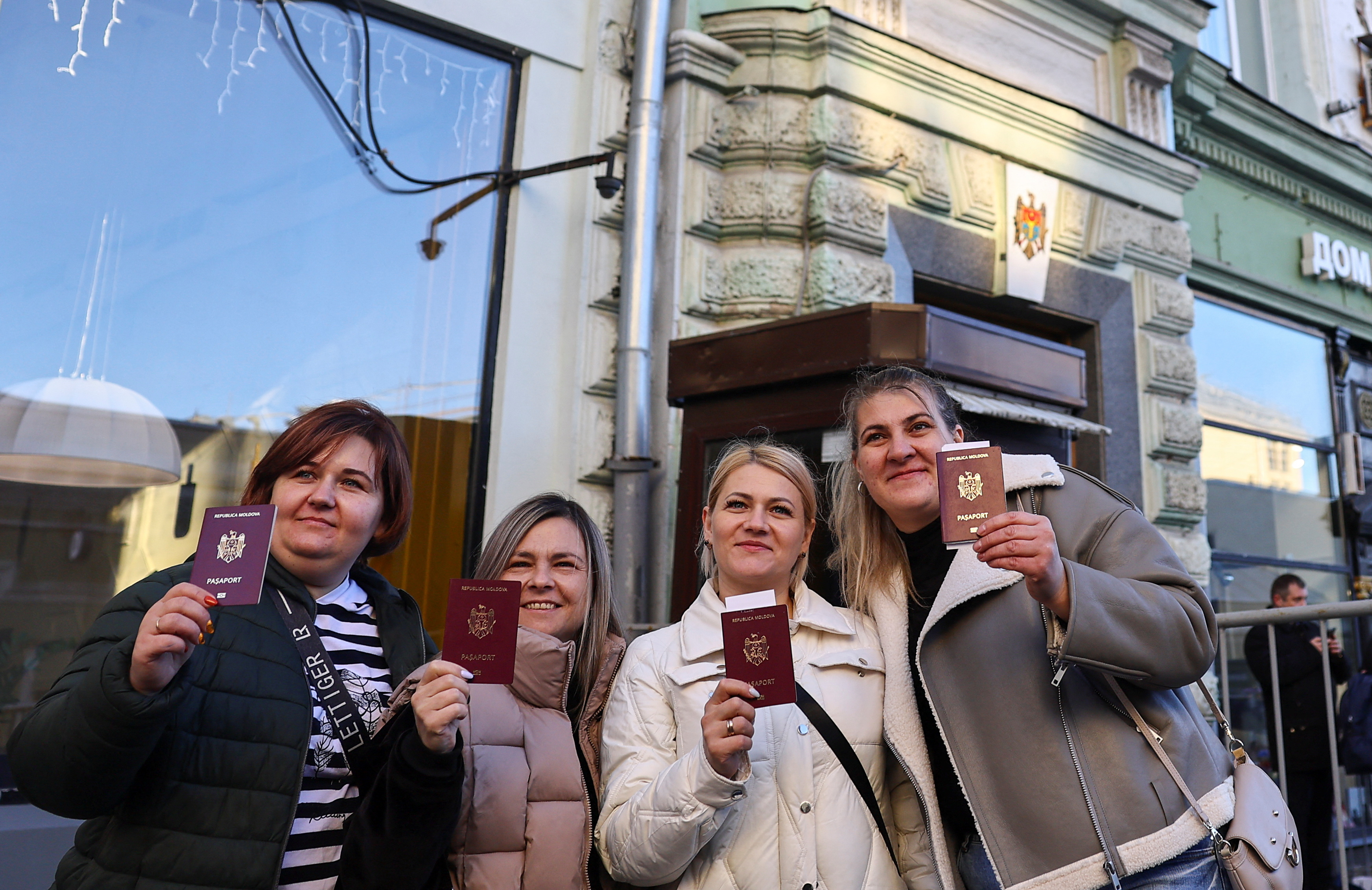 Women show their Moldovan passports while posing for a picture outside a polling station