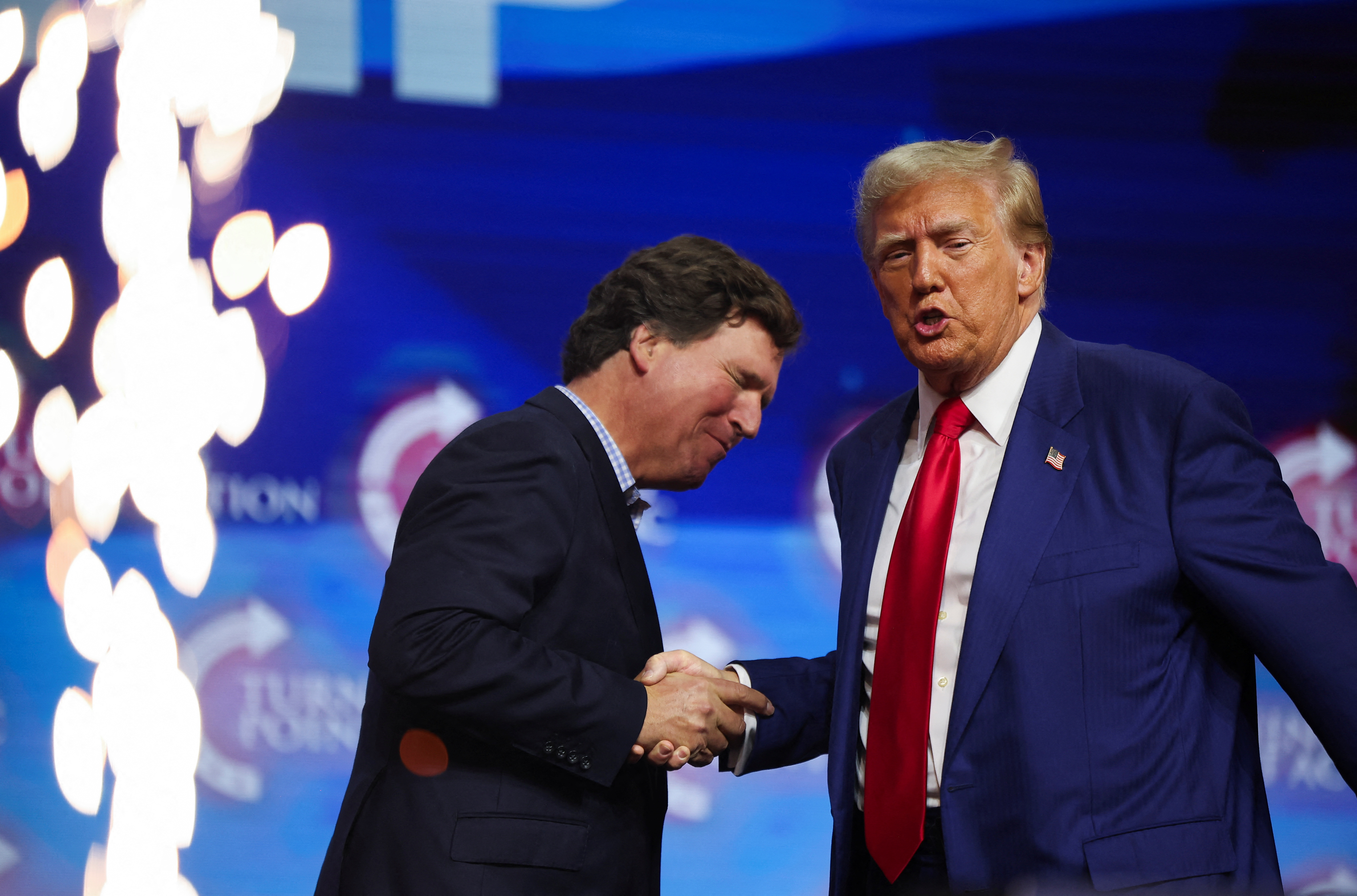 Republican presidential nominee and former U.S. President Donald Trump shakes hands with Tucker Carlson at a campaign event sponsored by conservative group Turning Point USA, in Duluth, Georgia, U.S., October 23, 2024. REUTERS/Carlos Barria