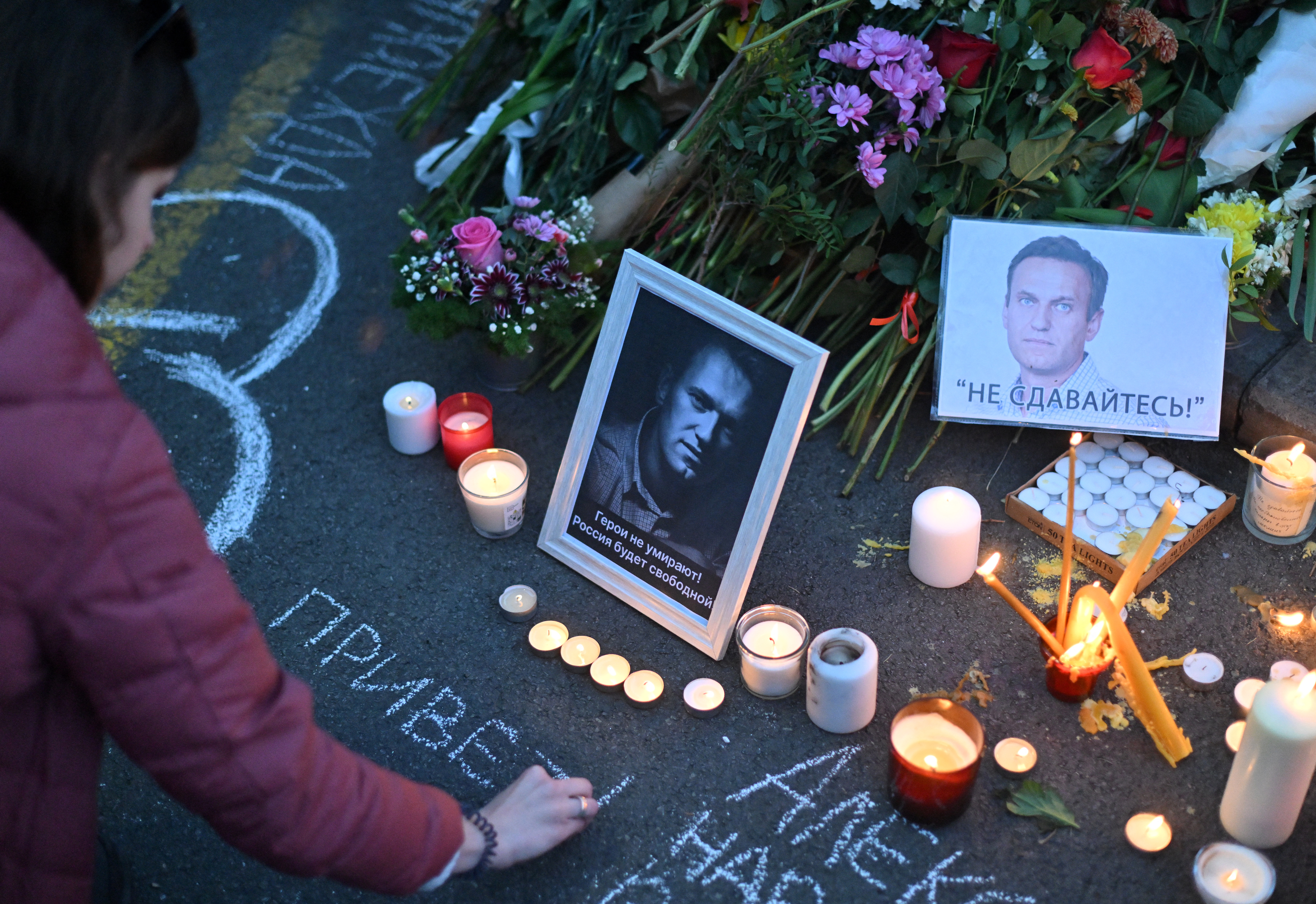 A woman uses chalk to write a message by a portrait of Alexey Navalny displayed amongst flowers and lit candles as protesters pay their respects outside the Russian Embassy in Belgrade, on February 16, 2024, following the news of Russian opposition leader and political activist Alexey Navalny's death at the Arctic prison where he was serving a 19-year-term. (Photo by OLIVER BUNIC / AFP)