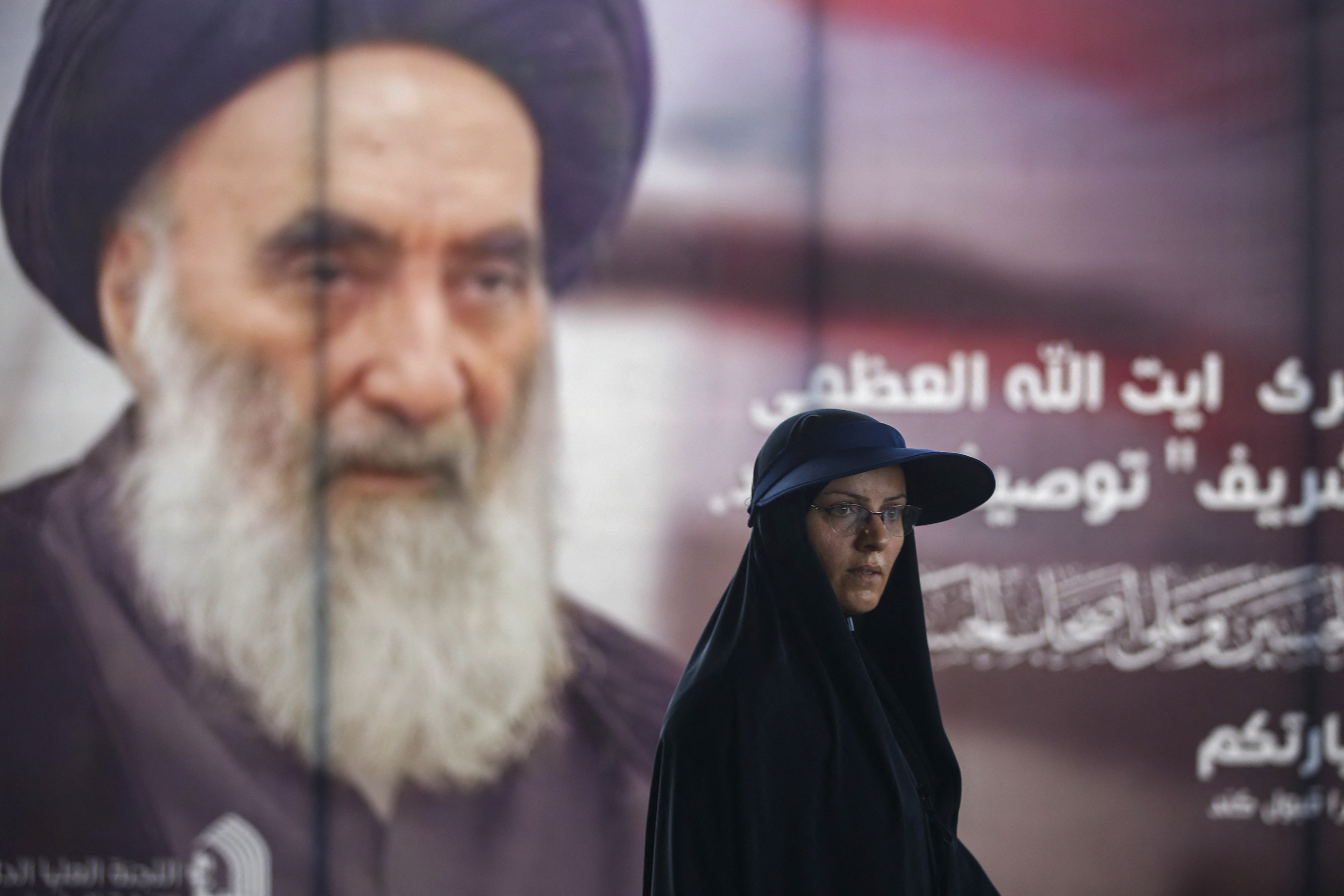 Woman dressed in black stands in front a poster of Ayatollah Sistani