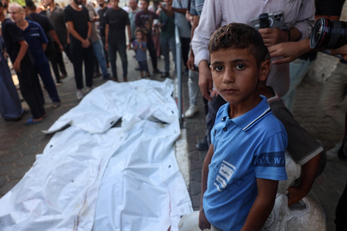 A boy stands with others near the bodies of people killed in a house hit by an Israeli strike