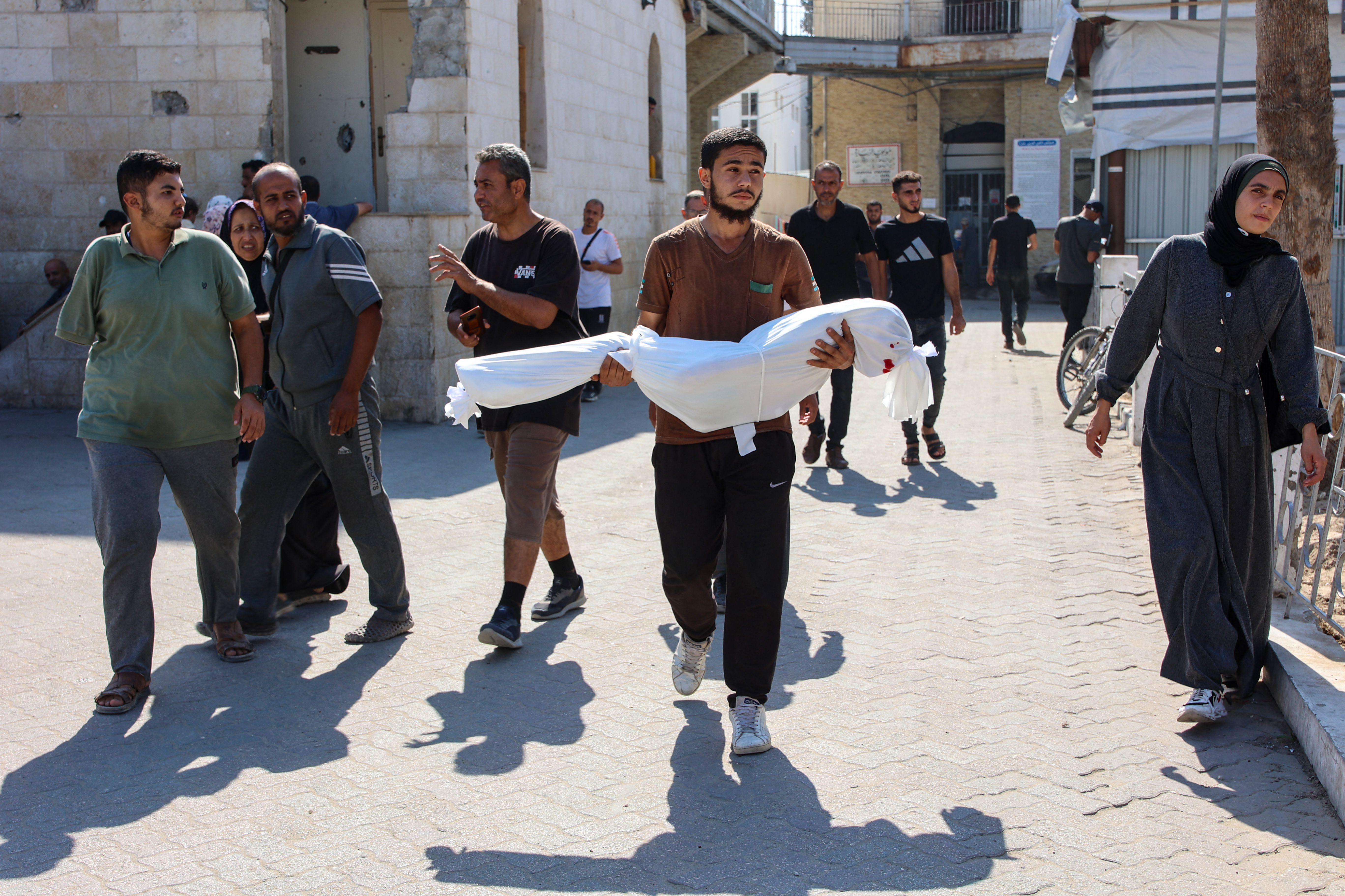 TOPSHOT - A relative carries the shrouded body of ten-year-old Sama al-Debs, who was killed during an Israeli army operation in the Jabalia refugee camp in the central Gaza Strip, ahead of her funeral on October 18, 2024, amid the continuing war between Israel and the Palestinian militant group Hamas. (Photo by Omar AL-QATTAA / AFP)