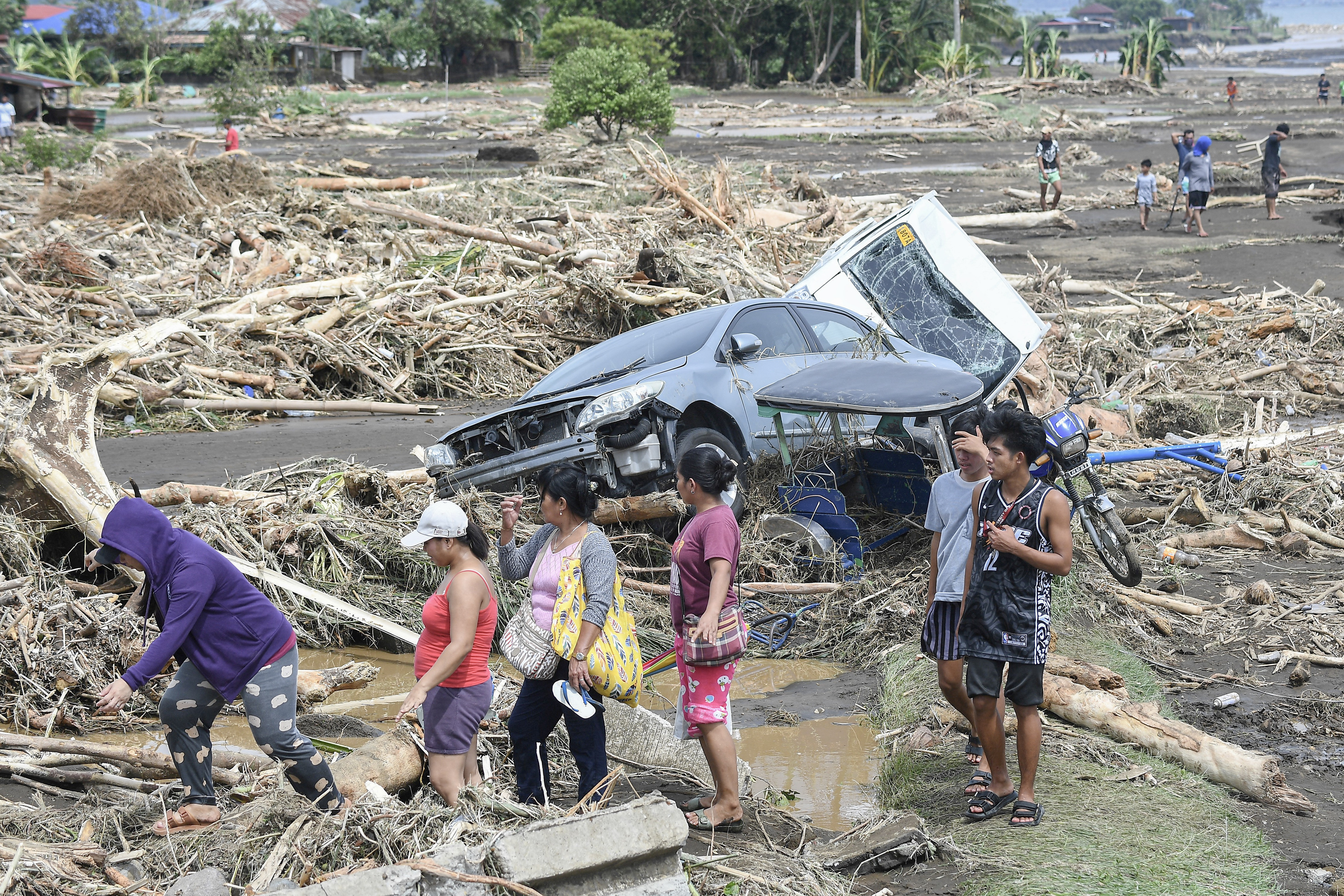 TOPSHOT - People walk past destroyed vehicles swept away along with debris of logs due to heavy rains brought about by Tropical Storm Trami in Laurel, Batangas province, south of Manila on October 25, 2024. Philippine rescue workers battled floodwaters on October 25 to reach residents still trapped on the roofs of their homes as Tropical Storm Trami moved out to sea after killing at least 40 people. (Photo by Ted ALJIBE / AFP)