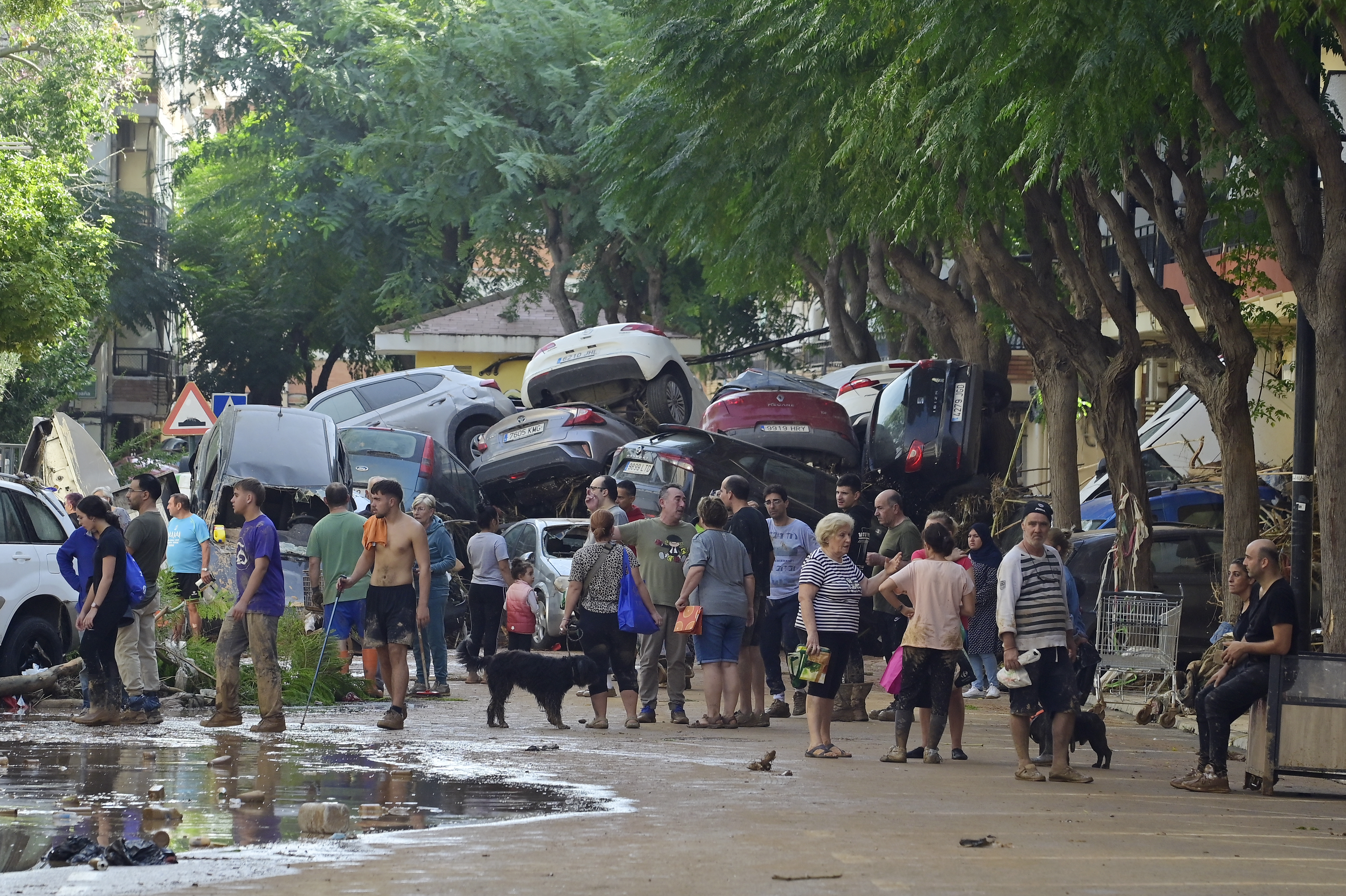 Residents gather in the street next to a pile of cars on October 31, 2024 after flash floods affected the town of Massanassa, in the region of Valencia, eastern Spain. - Rescuers raced on October 31, 2024 to find survivors and victims of once-in-a-generation floods in Spain that killed at least 95 people and left towns submerged in a muddy deluge with overturned cars scattered in the streets. About 1,000 troops joined police and firefighters in the grim search for bodies in the Valencia region as Spain started three days of mourning. Up to a year's rain fell in a few hours on the eastern city of Valencia and surrounding region on October 29 sending torrents of water and mud through towns and cities. (Photo by JOSE JORDAN / AFP)