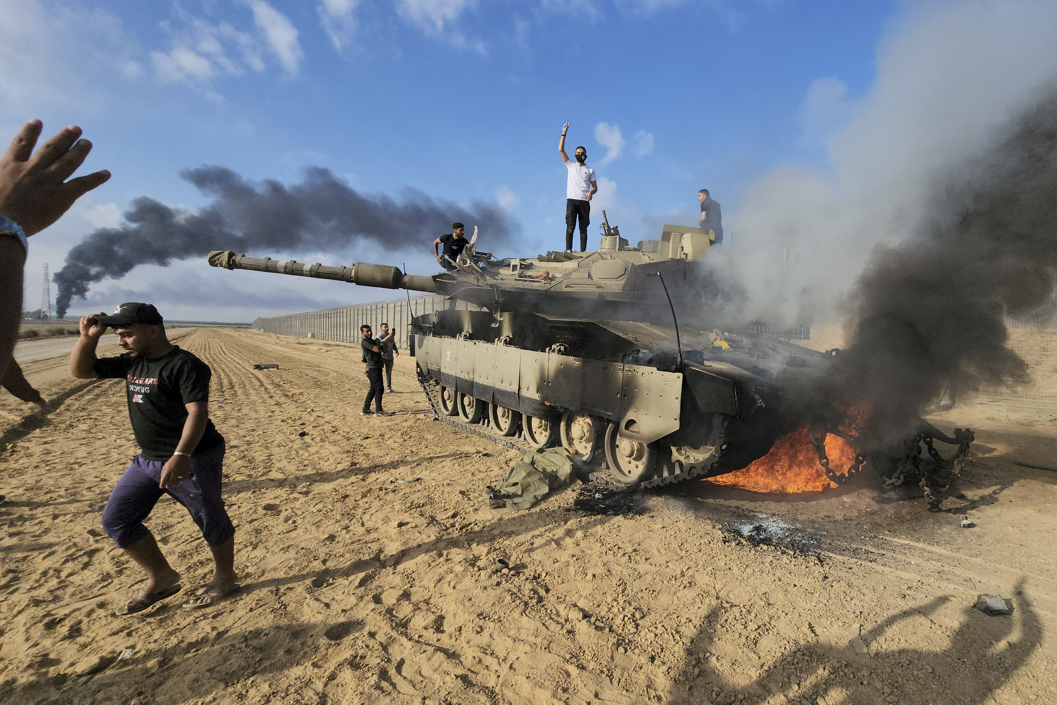 Palestinians celebrate by a destroyed Israeli tank at the Gaza Strip fence east of Khan Younis