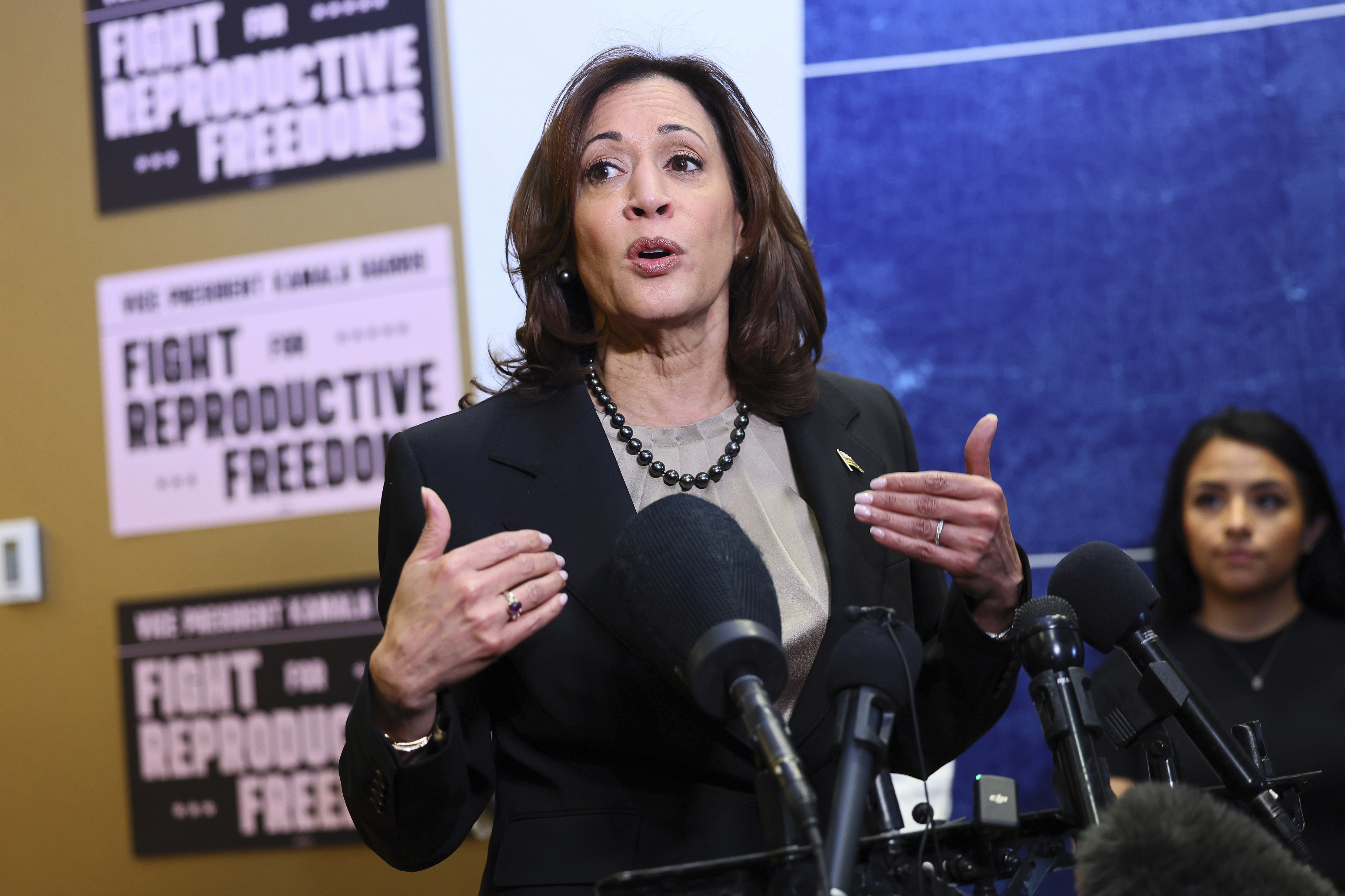 Kamala Harris speaks at a podium. Behind her is a wall that features posters about "reproductive freedom."