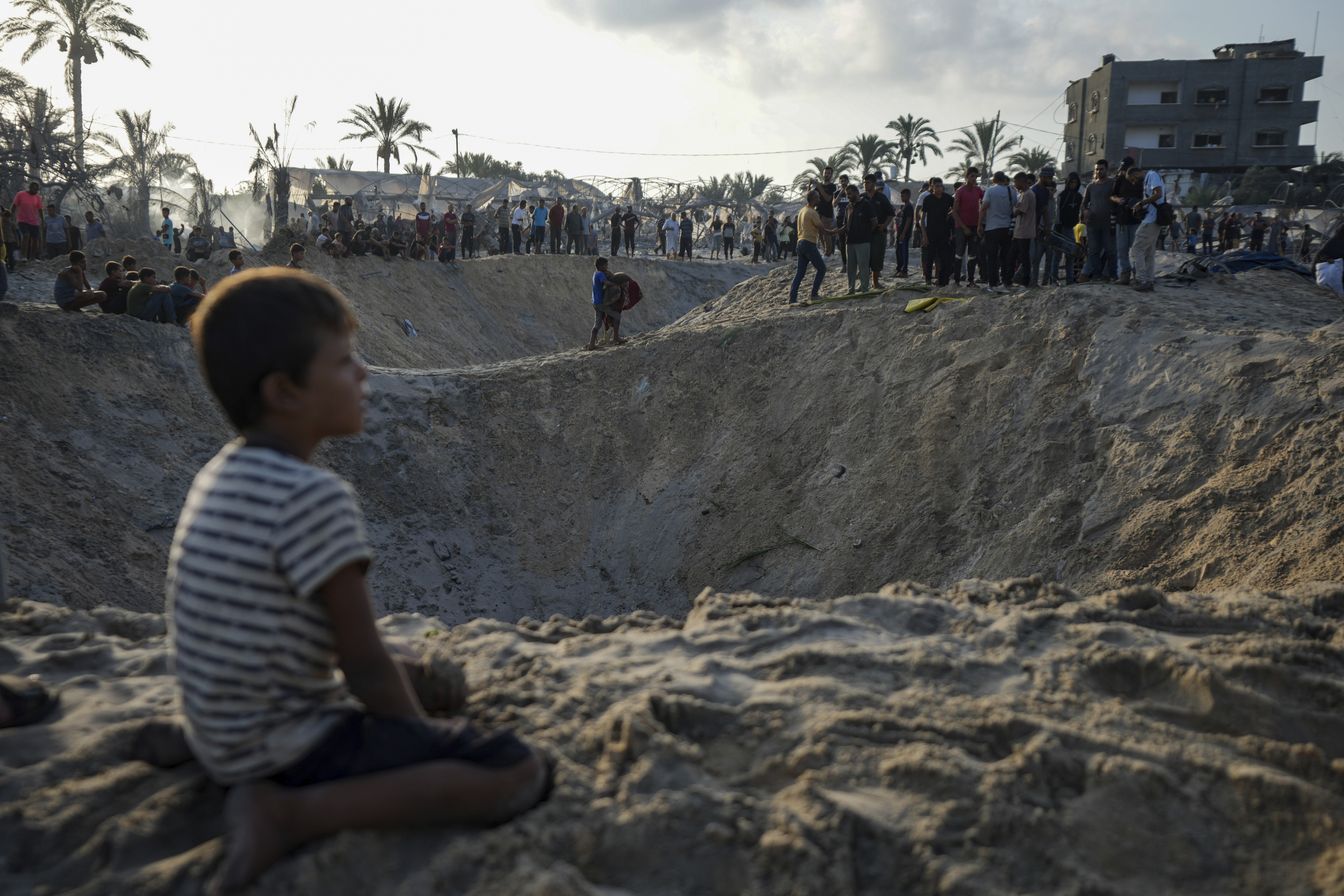 Palestinians look at the destruction after an Israeli airstrike on a crowded tent camp housing Palestinians displaced by the war in Muwasi,