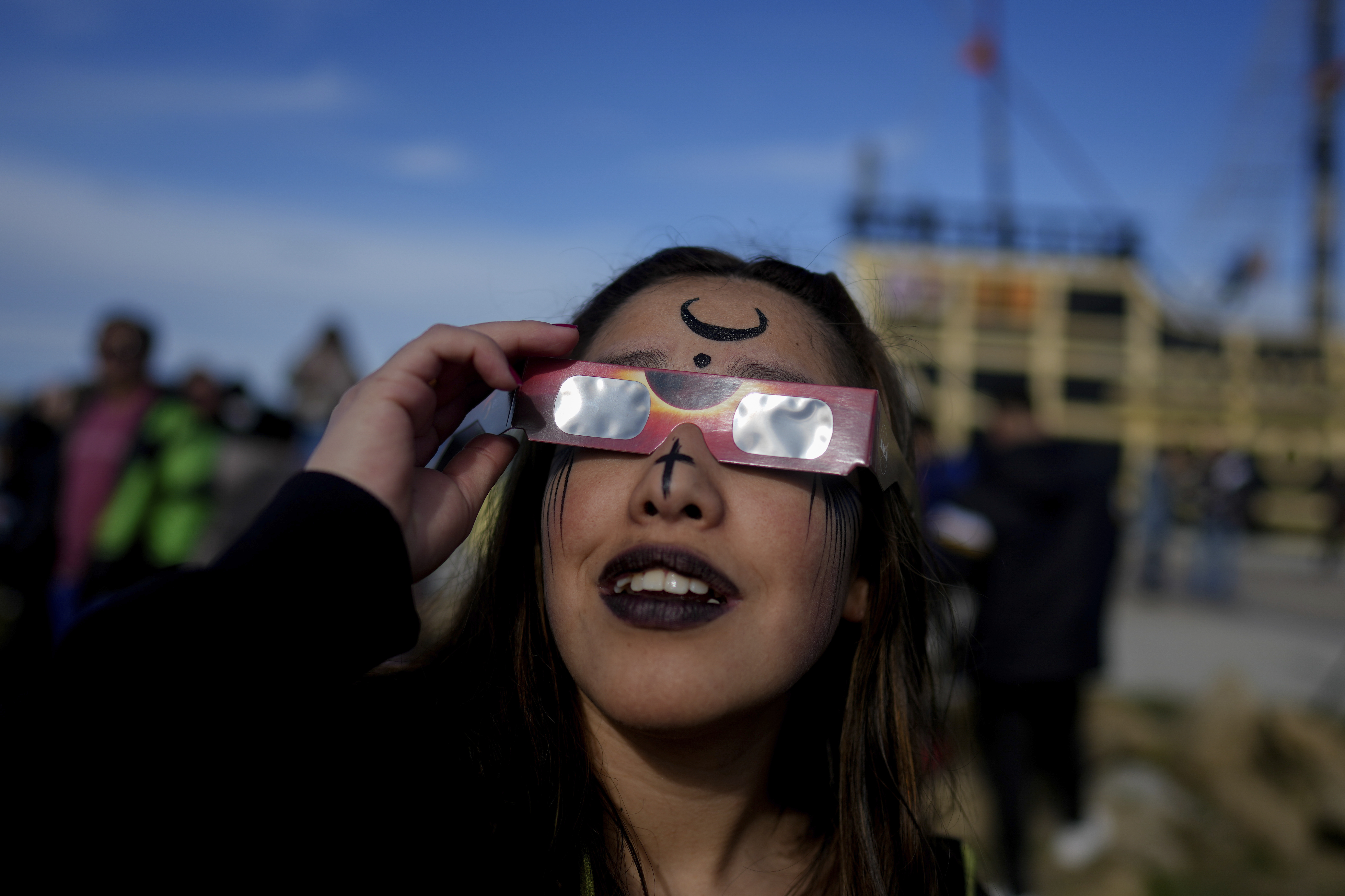 A person wears protective glasses to watch the eclipse and has a crescent drawn on her forehead.