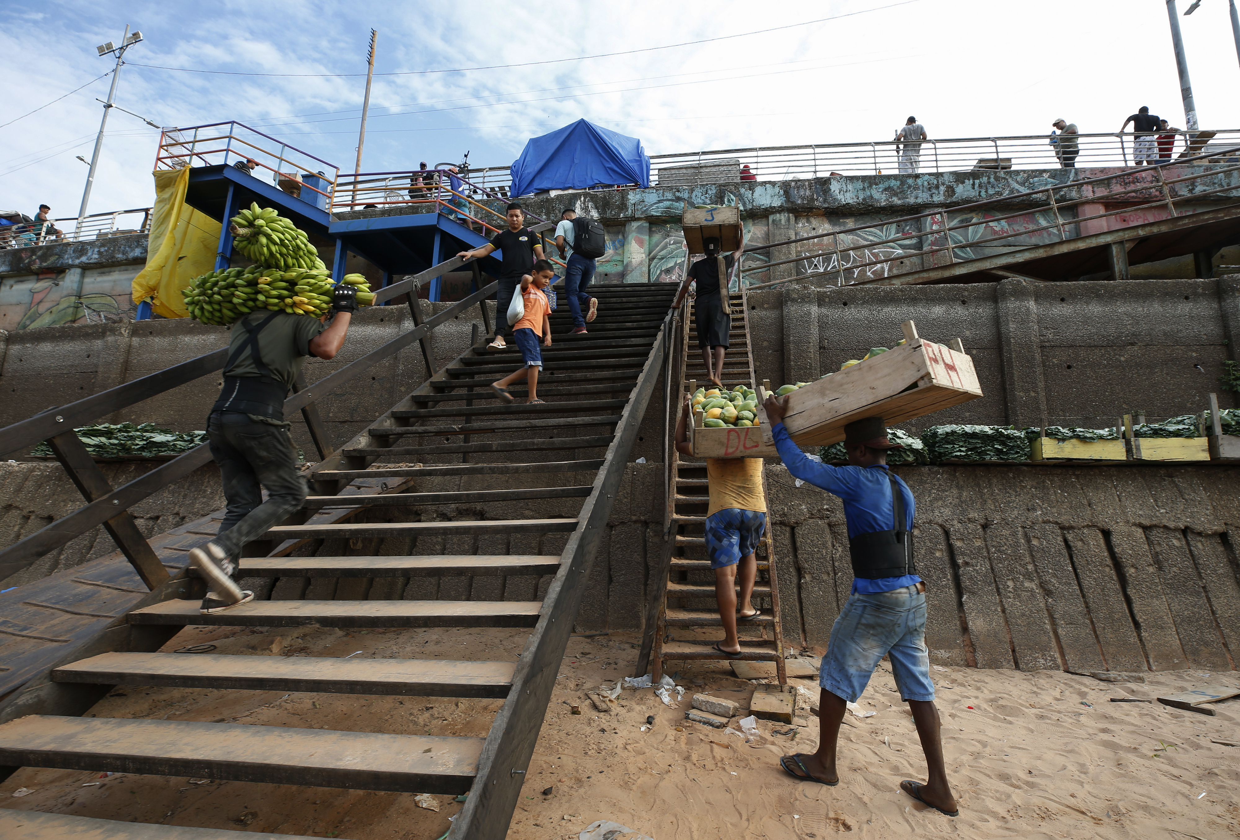 Porters carry goods up staircases set up next to stranded boats.
