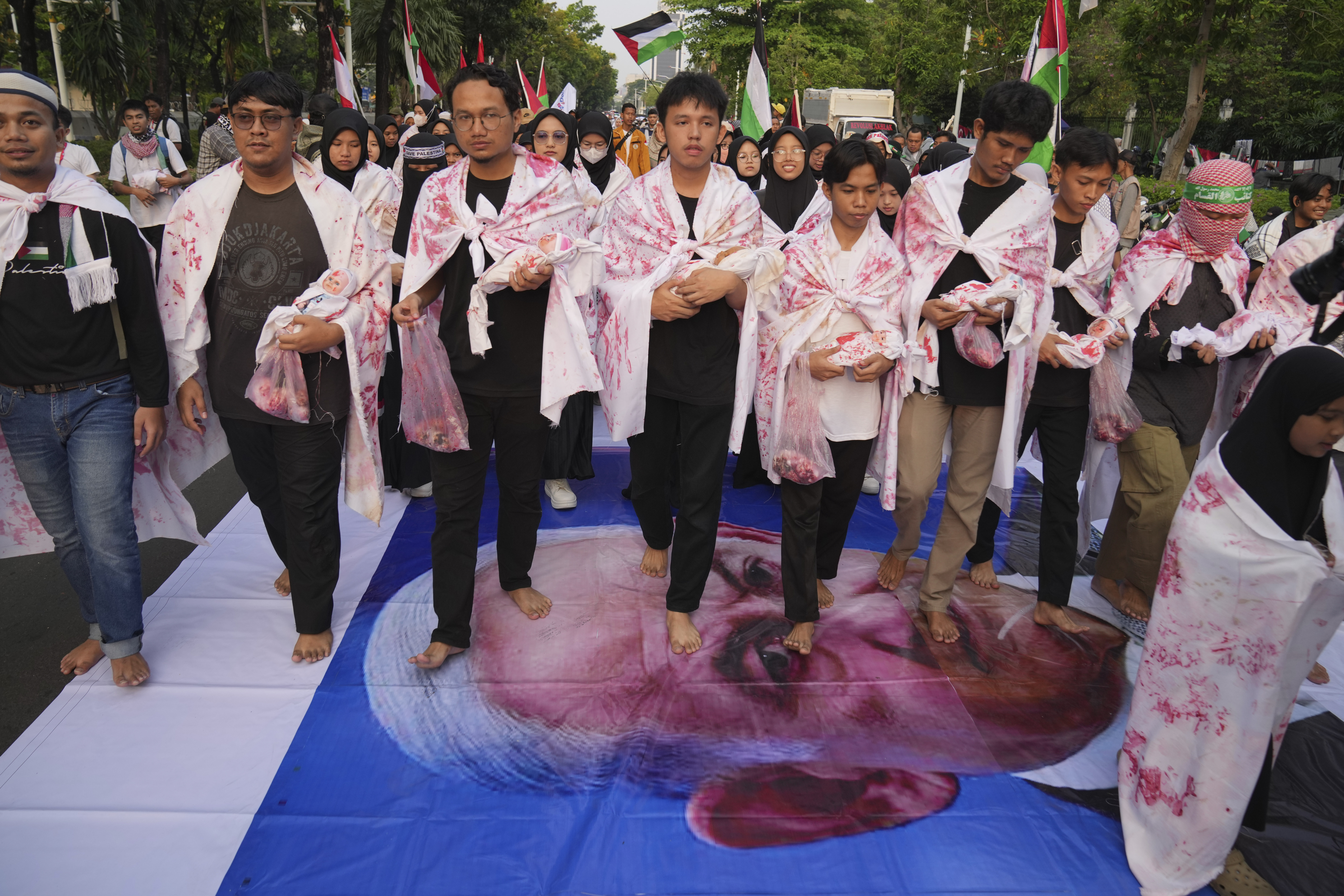 Protesters carrying dolls shrouded in white cloth to represent children killed in Gaza walk on a large banner of Israeli Prime Minister Benjamin Netanyahu during a rally supporting the Palestinians, outside the U.S. Embassy in Jakarta, Indonesia, Sunday, Oct. 6