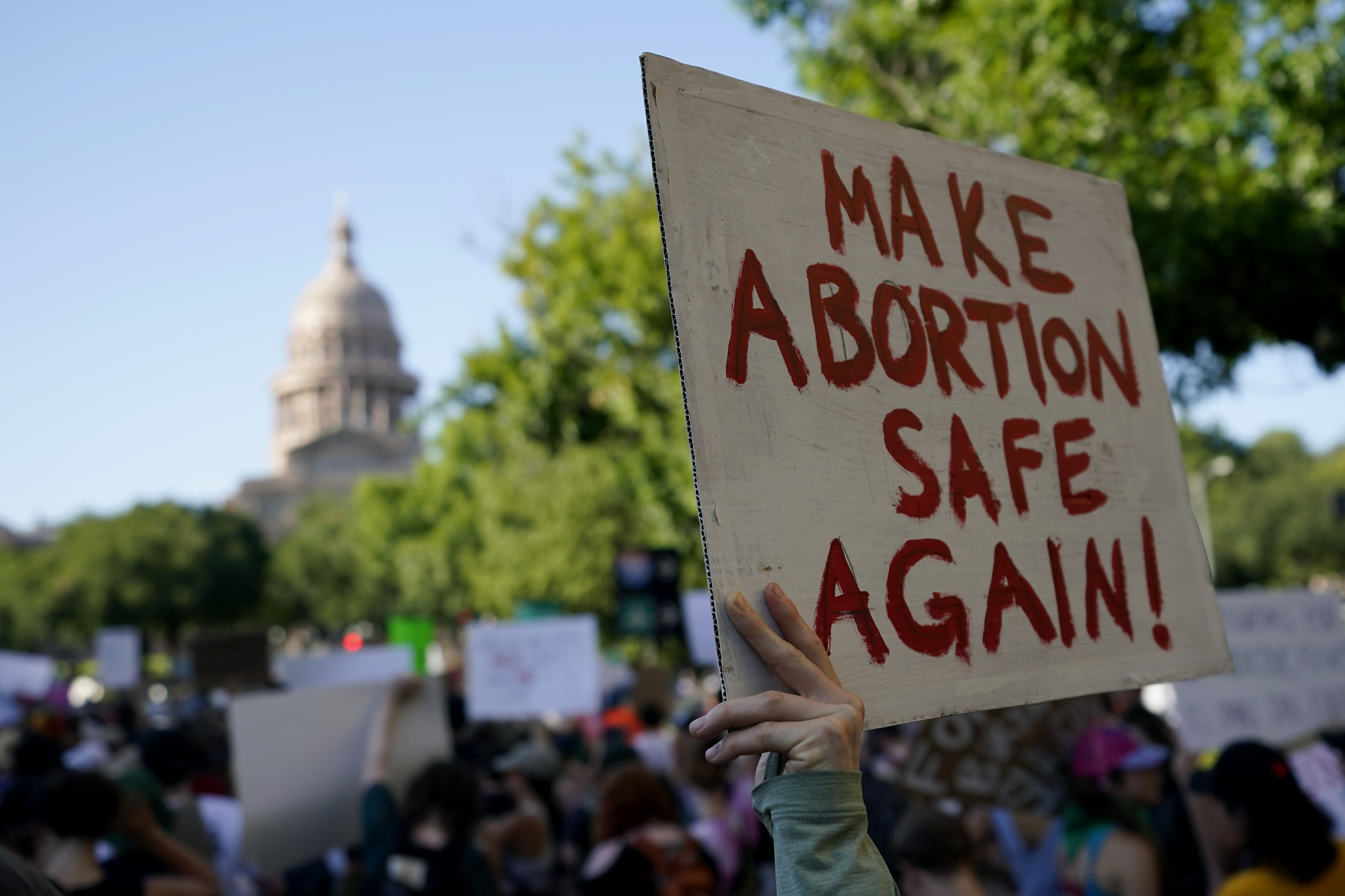 A protester holds up a sign that says, "Make Abortion Safe Again," as the Texas state capitol looms in the background.
