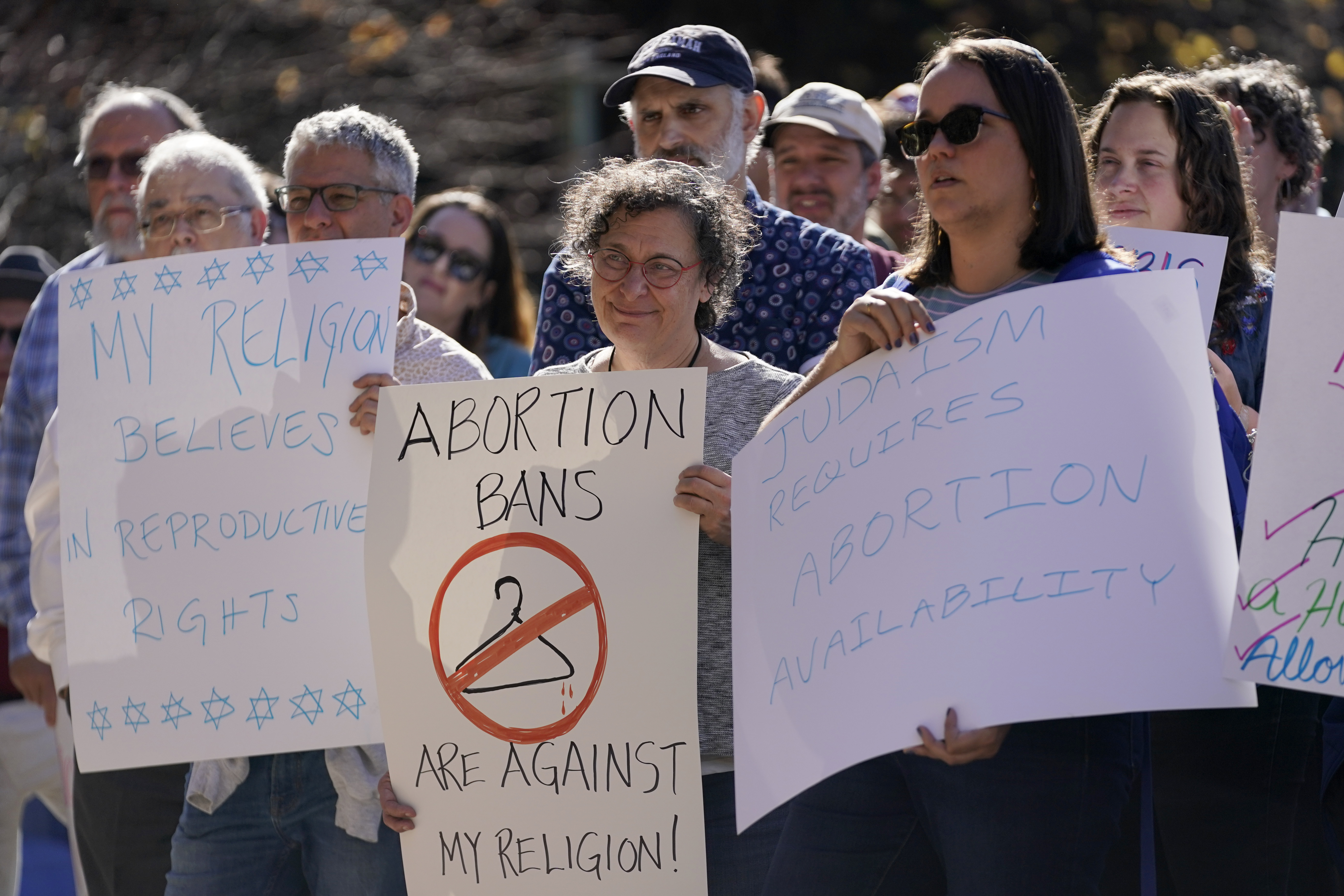 Protesters hold up hand-written signs warning about the dangers of abortion bans, including one that reads: "Abortion bans are against my religion," with a clothes hanger crossed out.