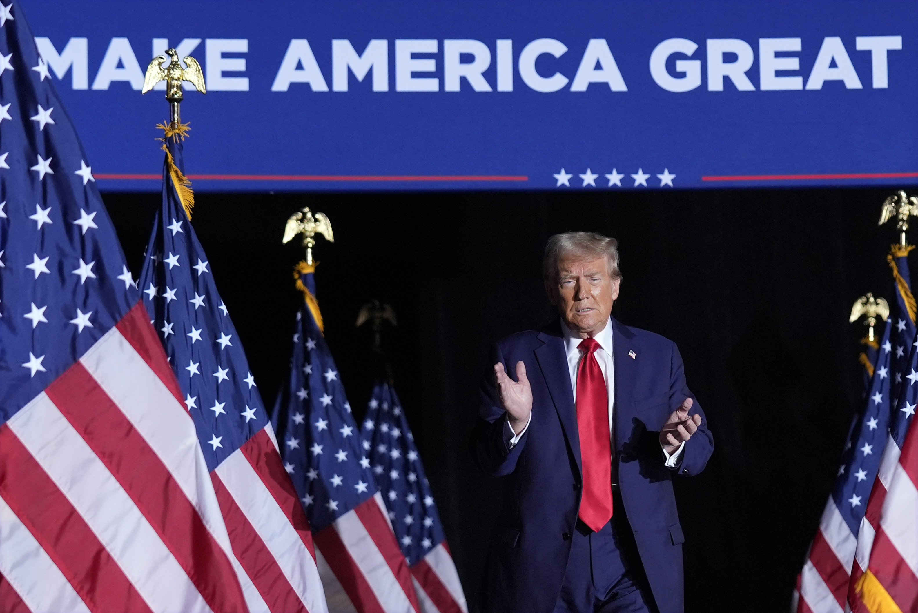 Donald Trump claps at a rally, as he walks past a row of US flags under a "Make America Great Again" sign.