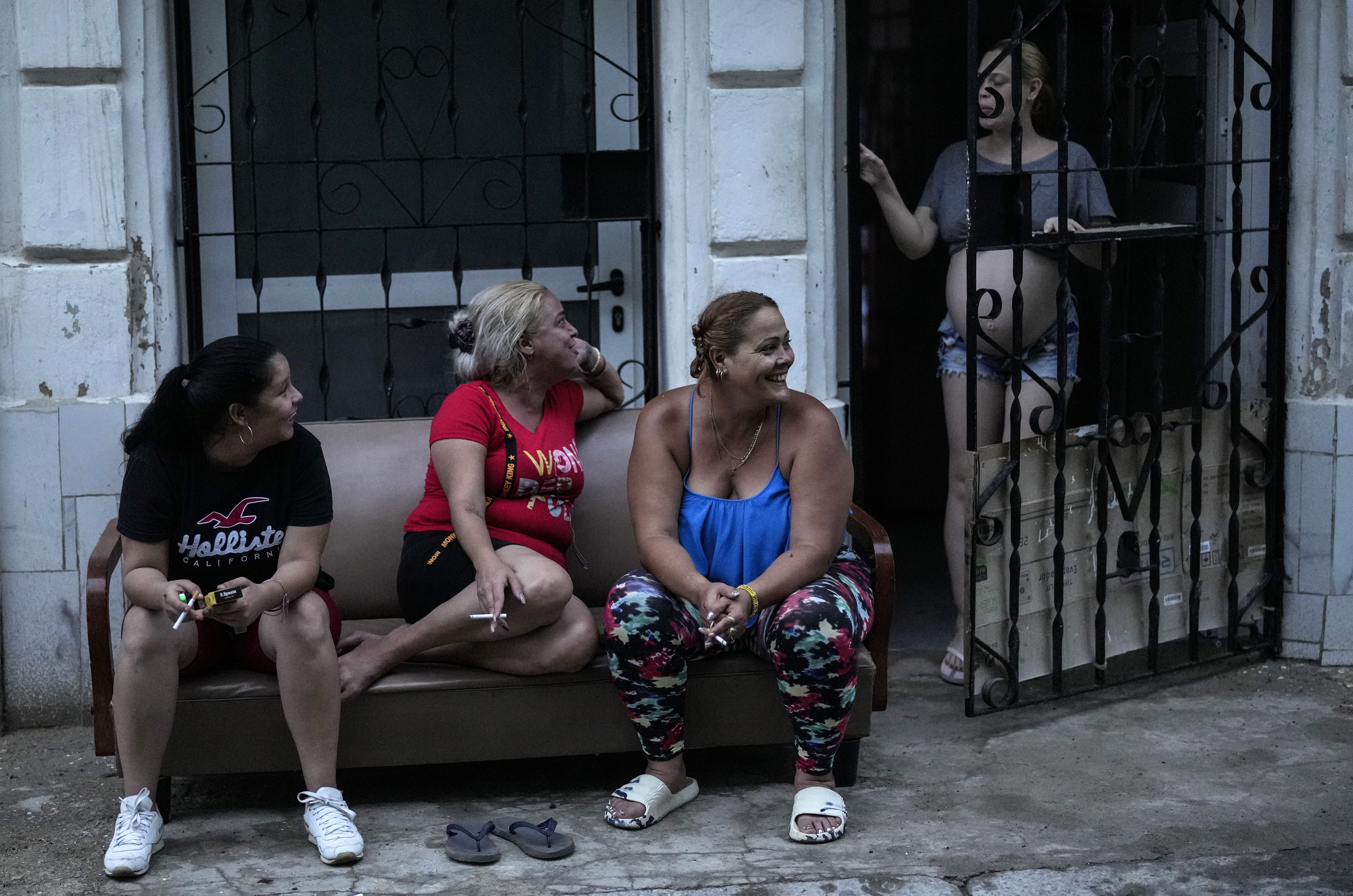 Three women outside a home in Havana, while another opens a metal gate leading inside.
