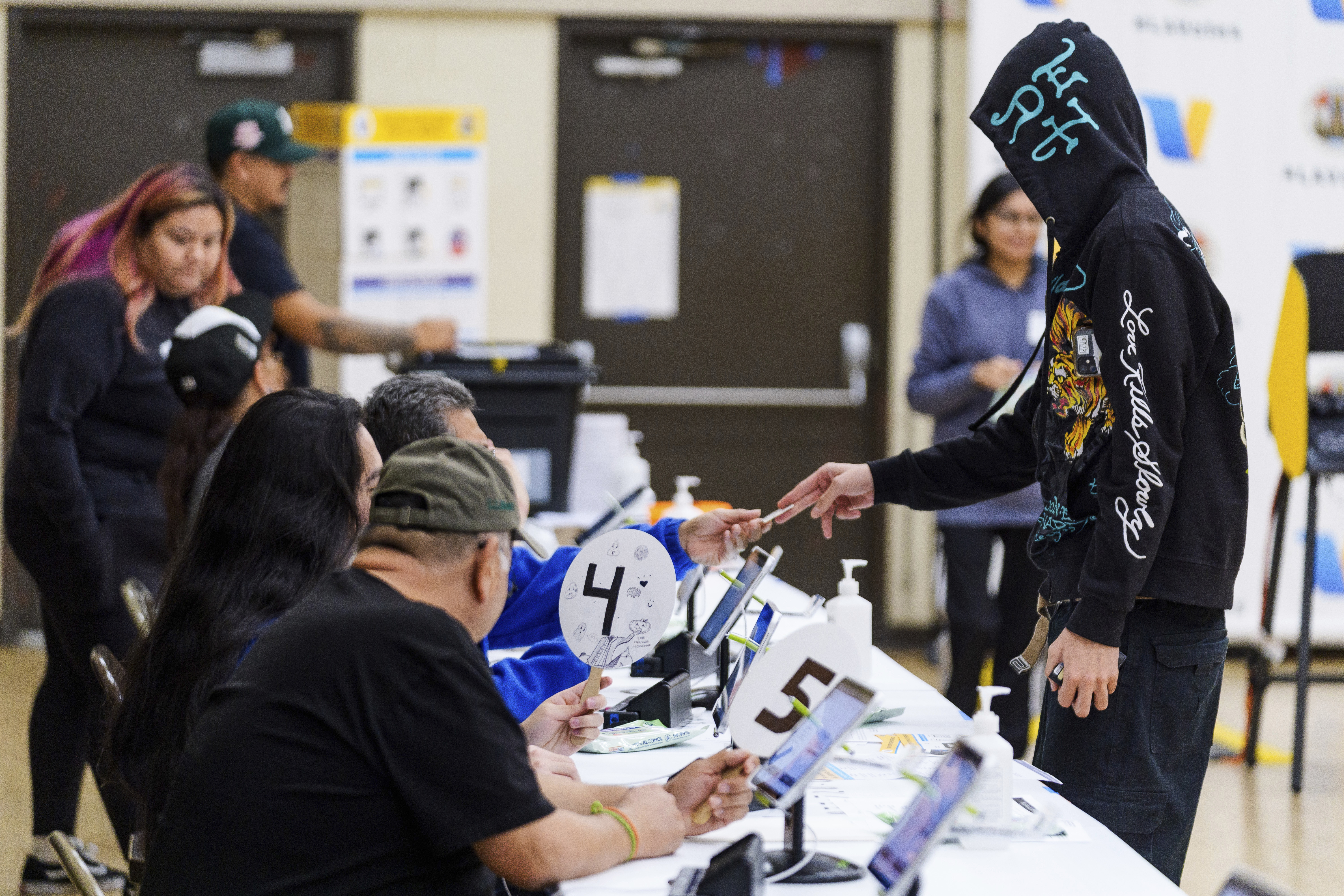 A man in a hoodie walks up to a panel of election worker sitting at a long table to vote.