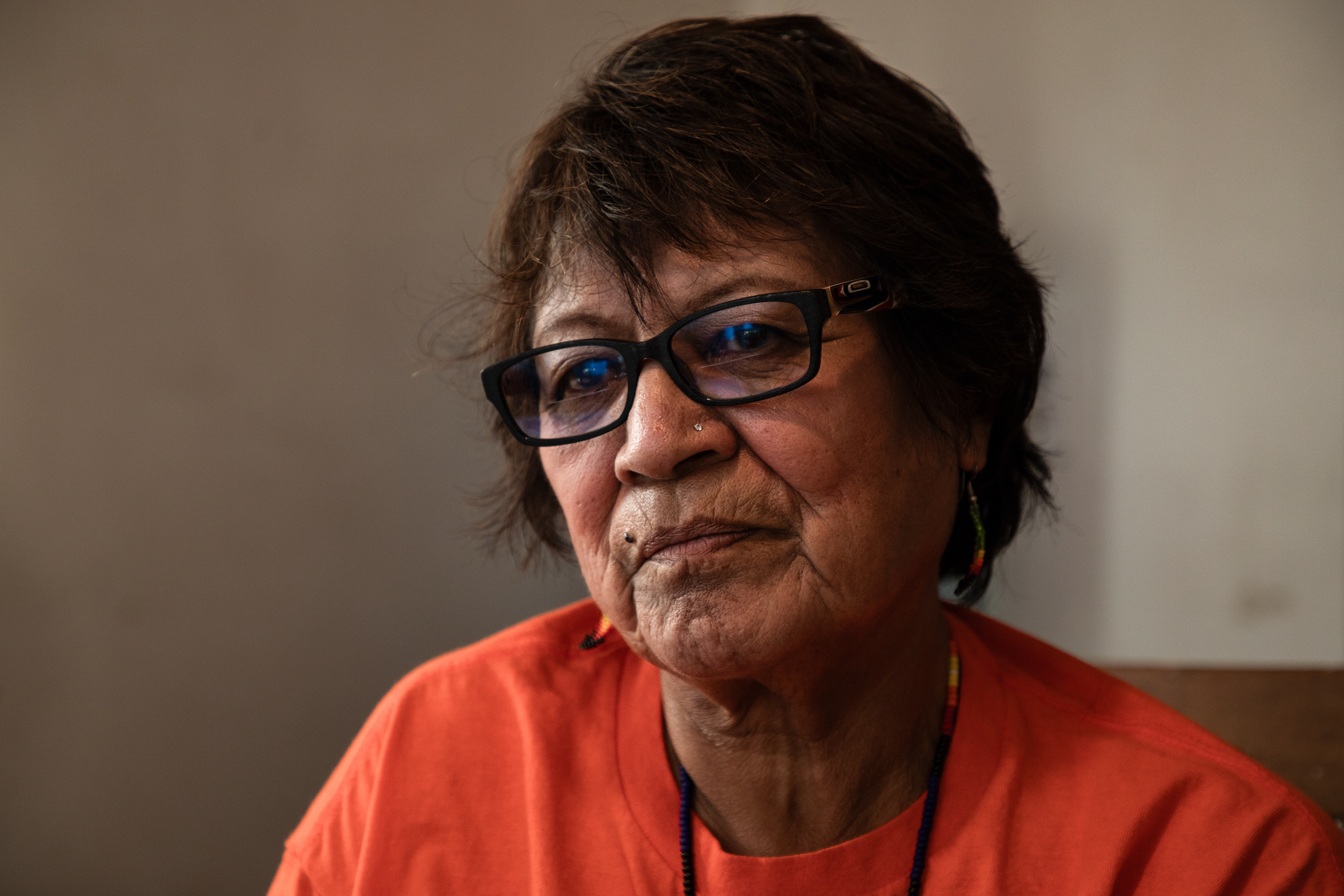 Martha Cardinal sits in her home, wearing an orange t-shirt and glasses