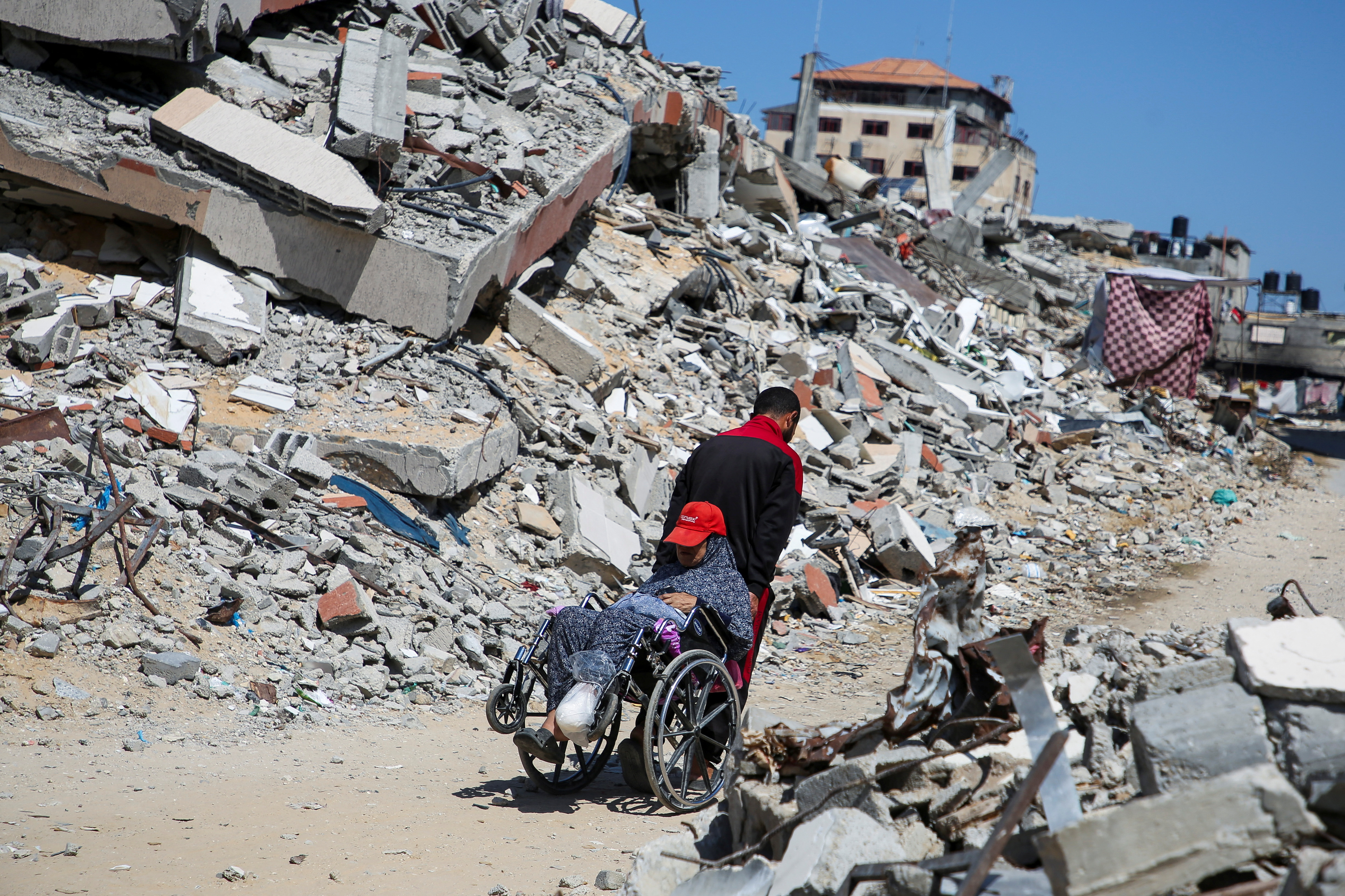 A Palestinian man assists a woman in a wheelchair past the rubble of a house destroyed in the Israel's military offensive, amid the Israel-Hamas conflict, in Khan Younis, in the southern Gaza Strip, September 26, 2024. REUTERS/Hatem Khaled