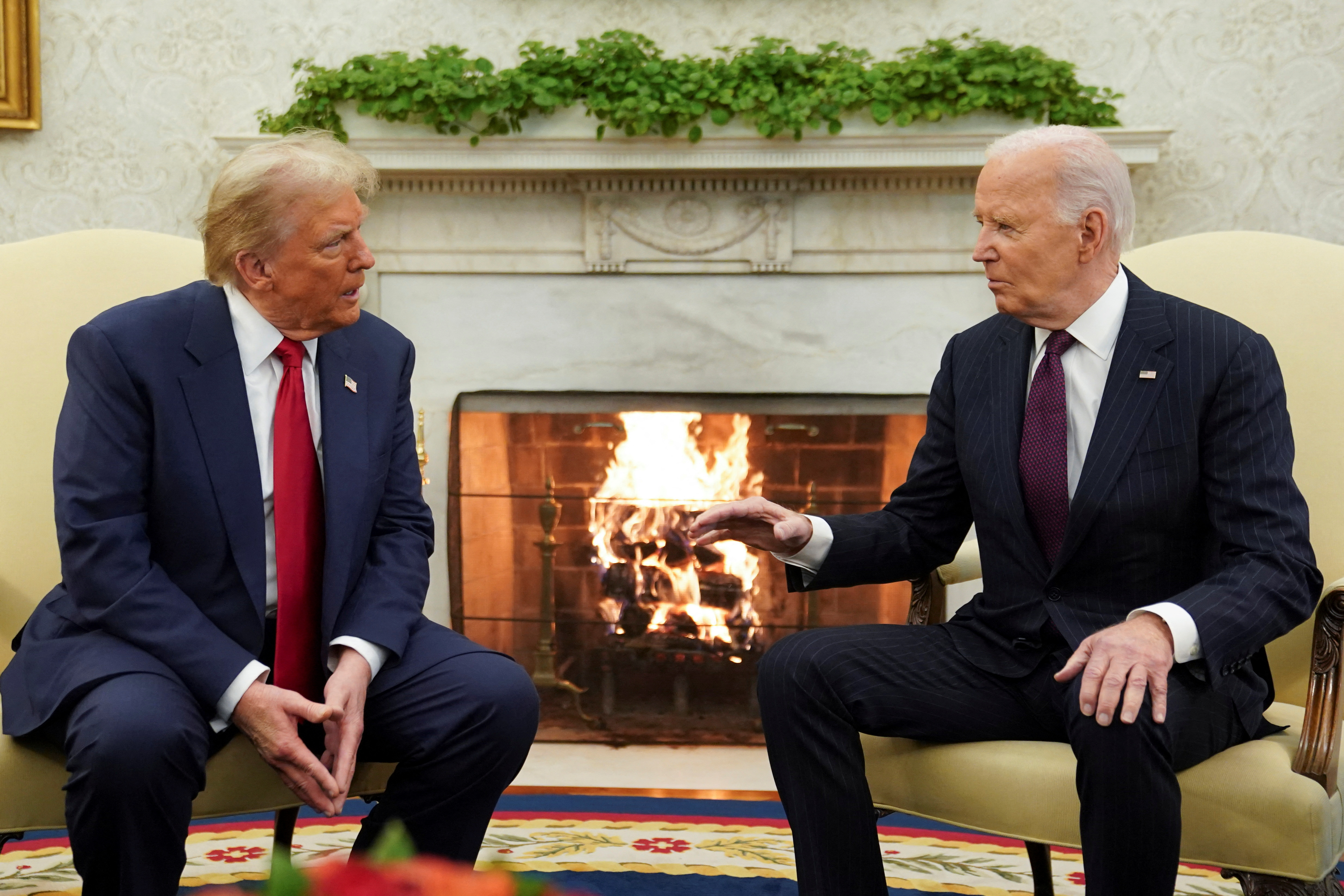 Donald Trump and Joe Biden sit in the Oval Office, in front of a roaring fireplace