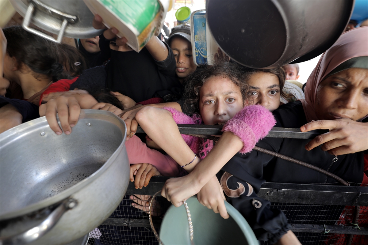 Palestinians, including children, living in the Nuseirat refugee camp wait with empty pots to receive food distributed by an aid organization