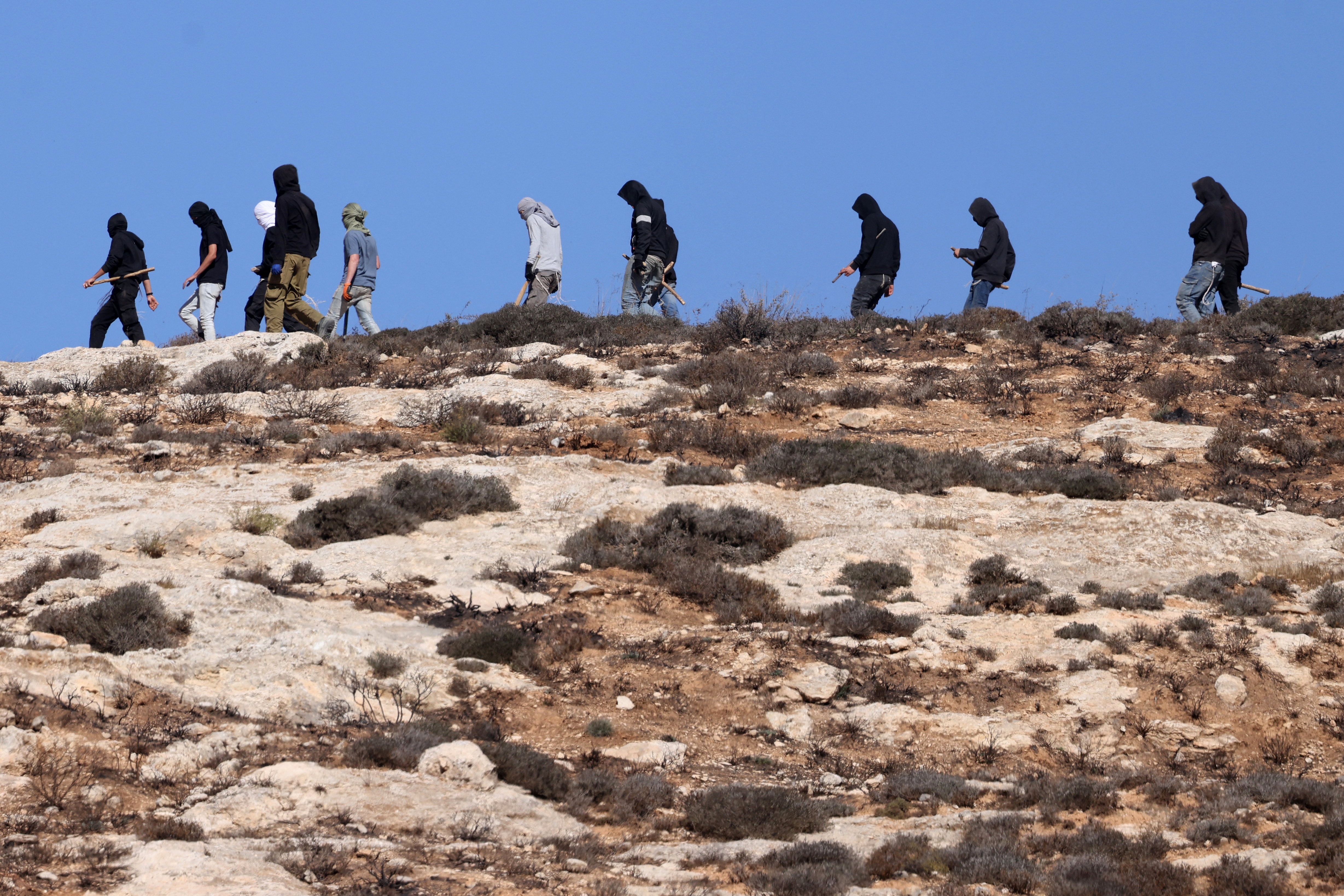 Israeli settlers patrol near the fields of Palestinian farmers in the village of Burqa