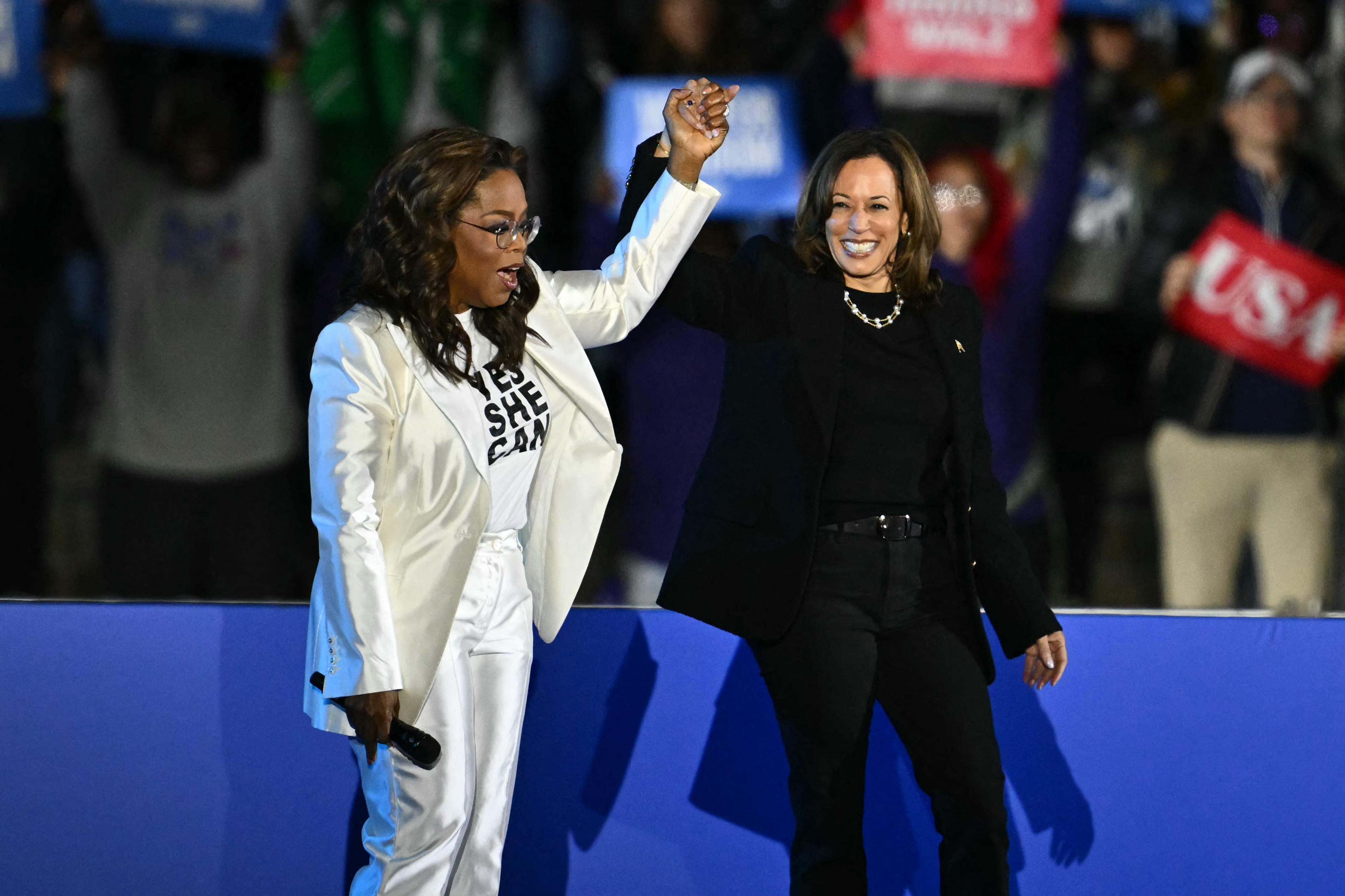 US producer and actress Oprah Winfrey holds up Democratic presidential candidate Kamala Harris's hand as she arrives on stage during a campaign rally on the Benjamin Franklin Parkway in Philadelphia