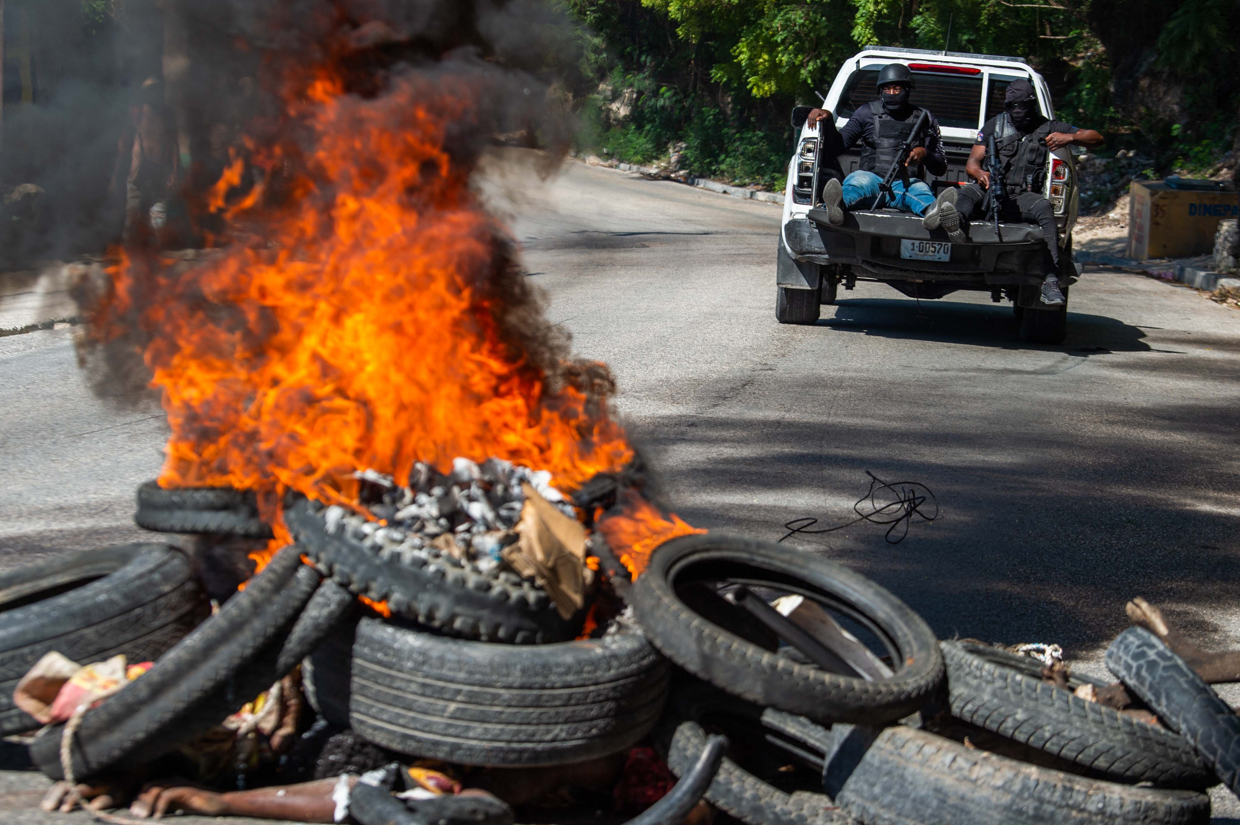EDITORS NOTE: Graphic content / Members of the Haitian National Police patrol as bodies of alleged gang members burn (in foreground) in Petion-Ville, a suburb of Port-au-Prince, Haiti, on November 19, 2024. - Police and civilian self-defense groups killed 28 alleged gang members in the Haitian capital Port-au-Prince in an overnight operation, authorities said Tuesday, as the government seeks to regain some control of the city. (Photo by Clarens SIFFROY / AFP)