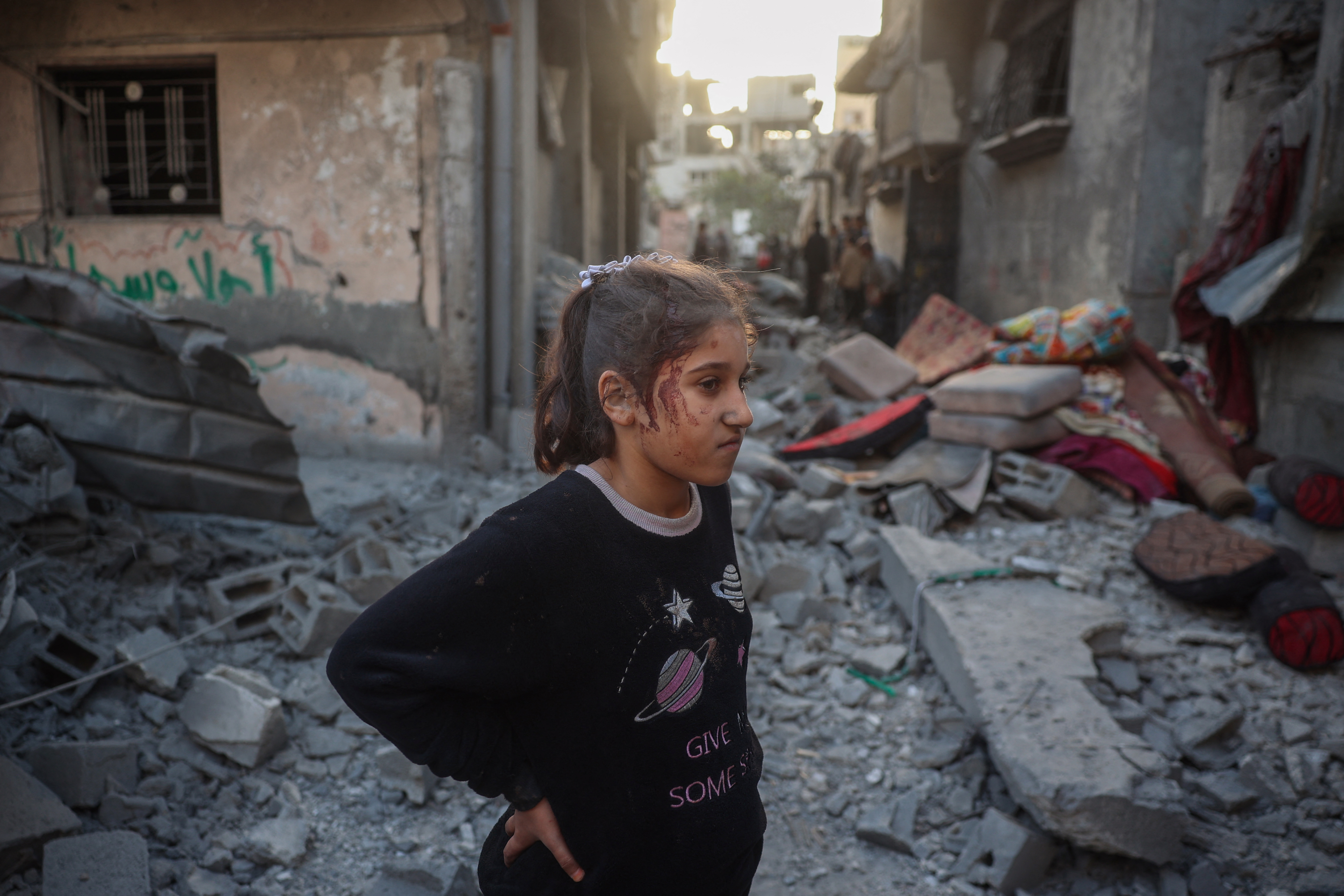 An injured girl stands amid the rubble of a house destroyed in an Israeli attack at the Bureij refugee camp
