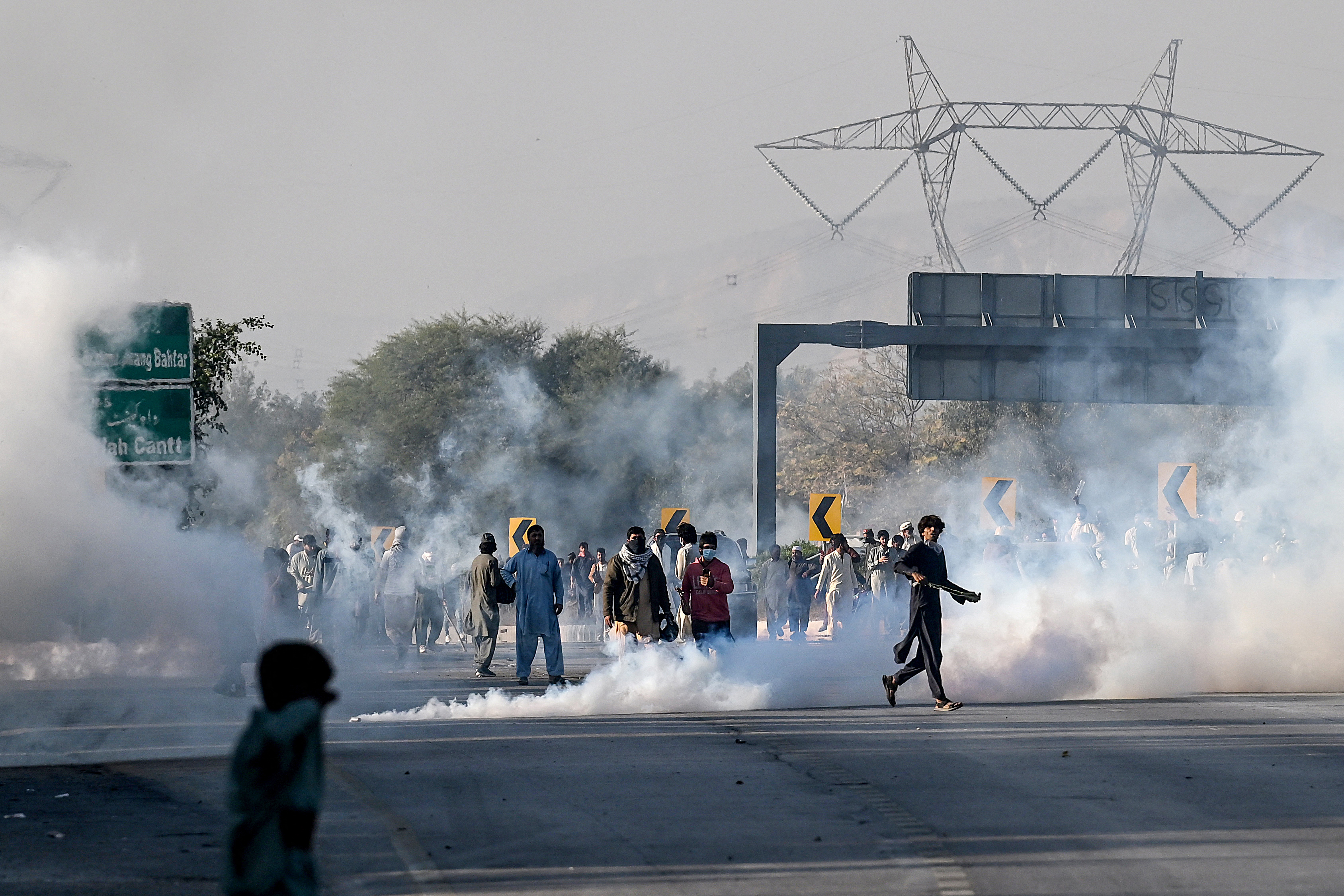 Members of jailed former prime minister Imran Khan's Pakistan Tehreek-e-Insaf (PTI) party attempt to throw back teargas shells fired by riot policemen as they protest during a march to Islamabad demanding Khan's release in Hasan Abdal in Punjab