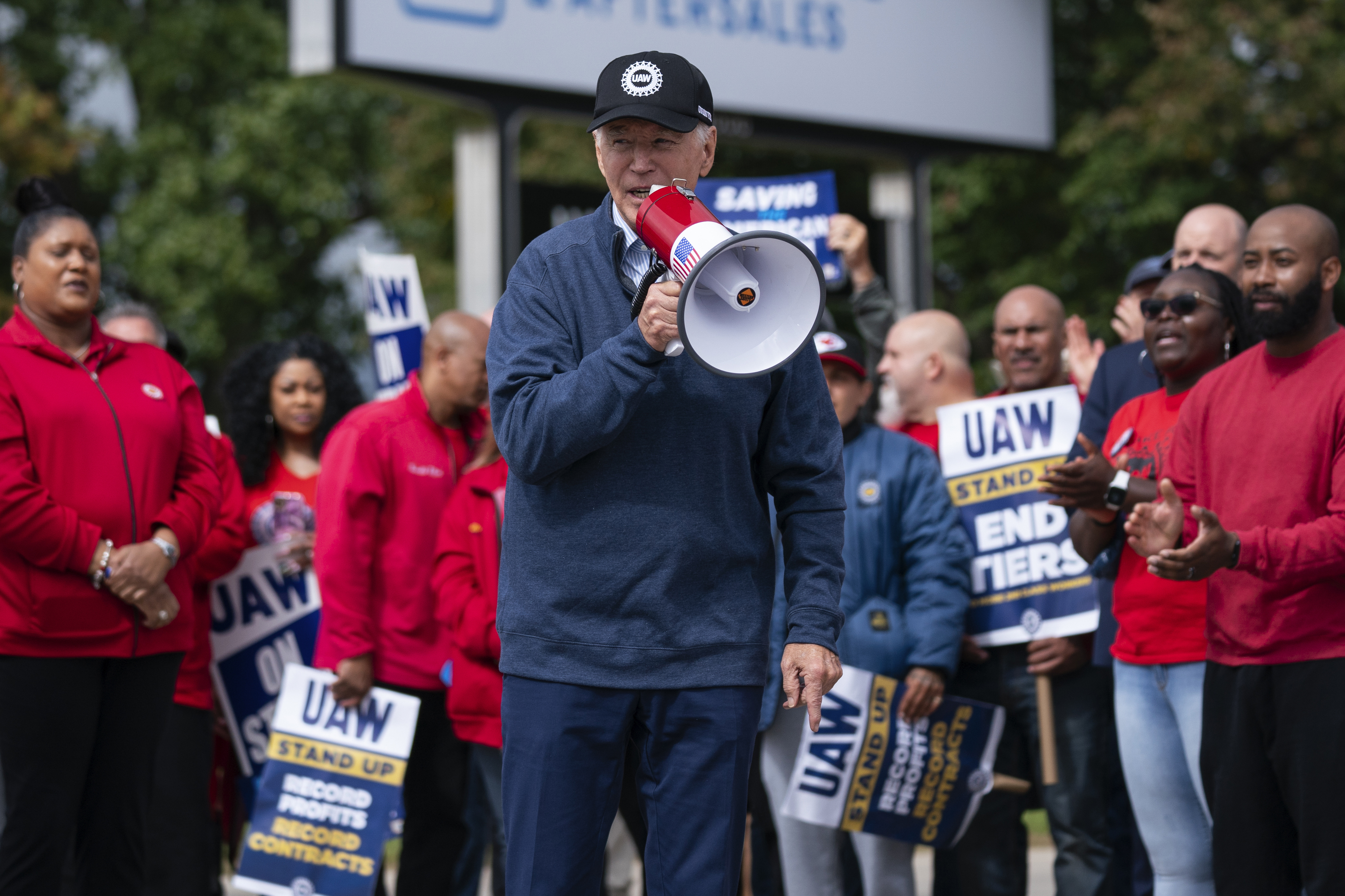 Joe Biden stands amid labour protesters, speaking into a microphone.