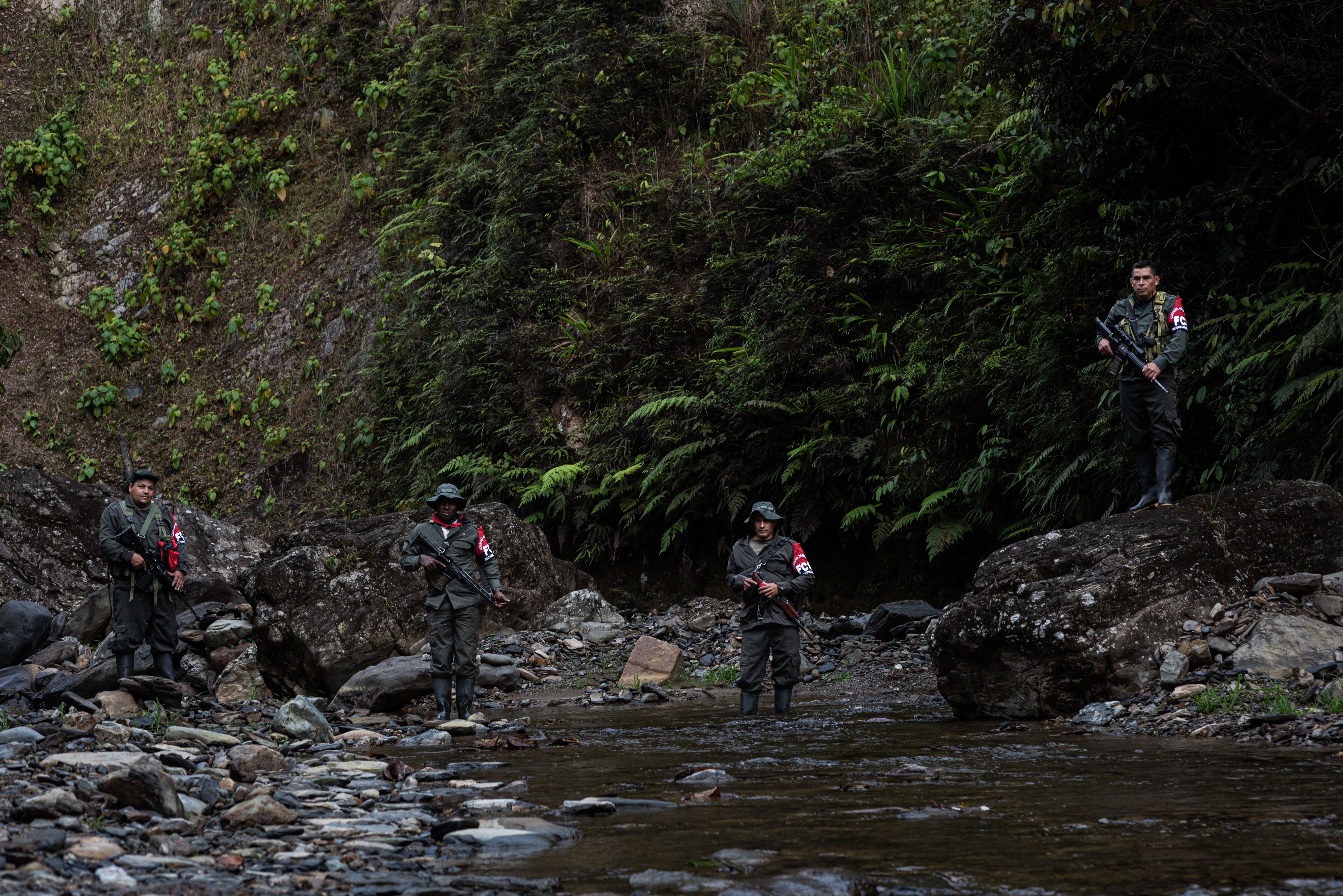 Comuneros del Sur fighters stand on the rocky shores of a creek in the Colombian jungle