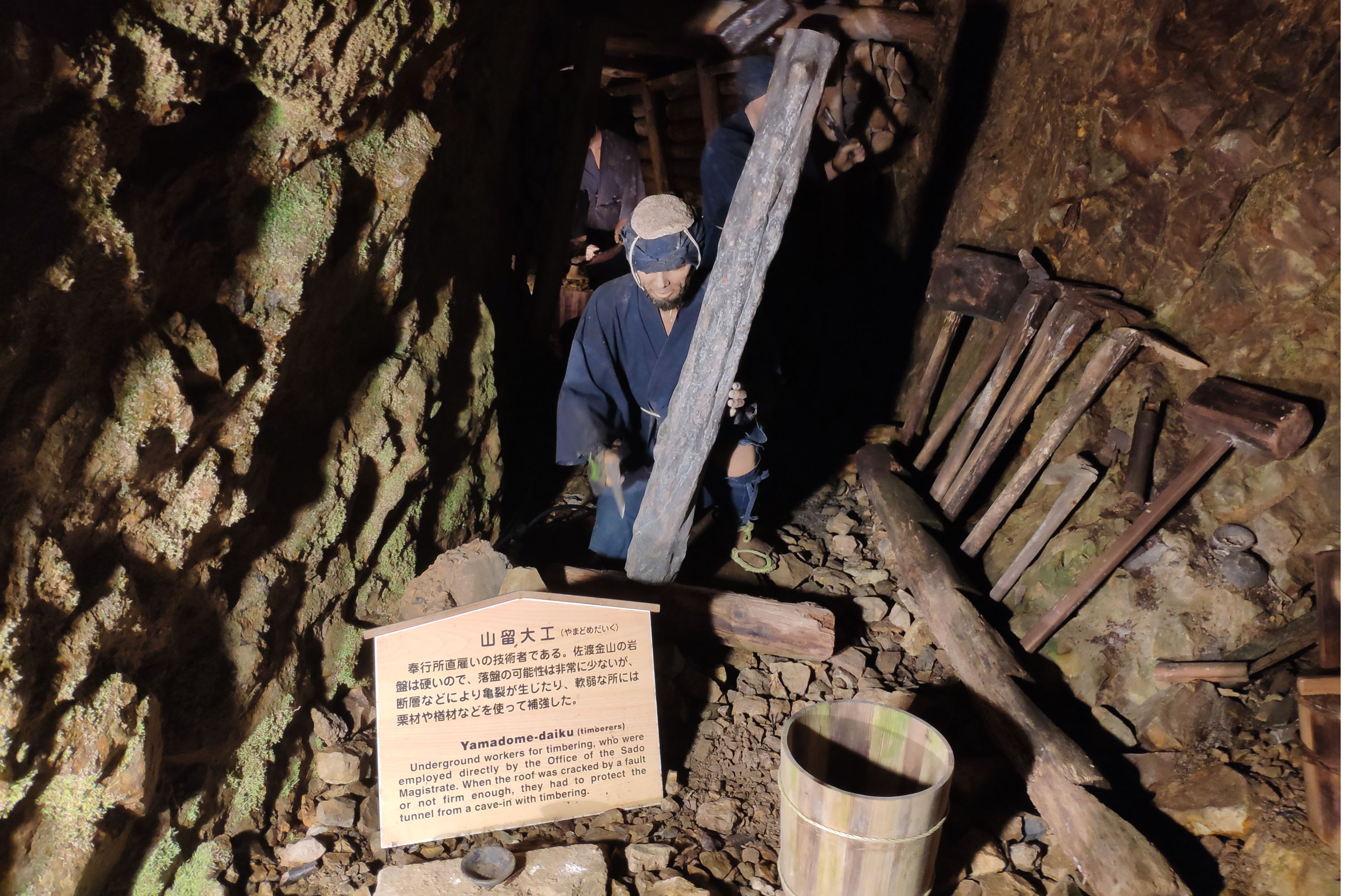 A photo inside a mine tunnel showing a mannequin holding a bar; a sign in Japanese and English is also visible