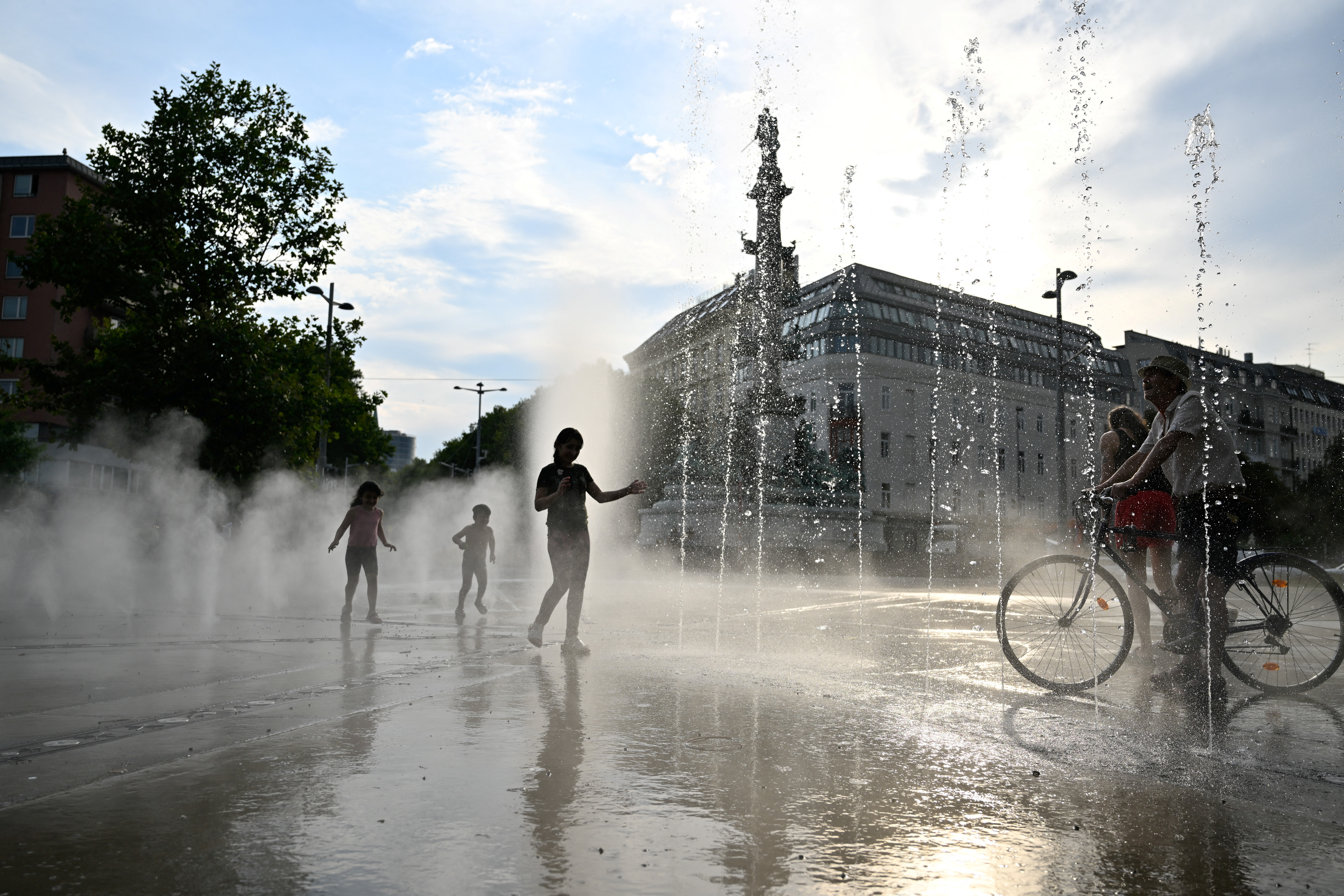 People cool off under a water sprinkler during a heat wave in Vienna