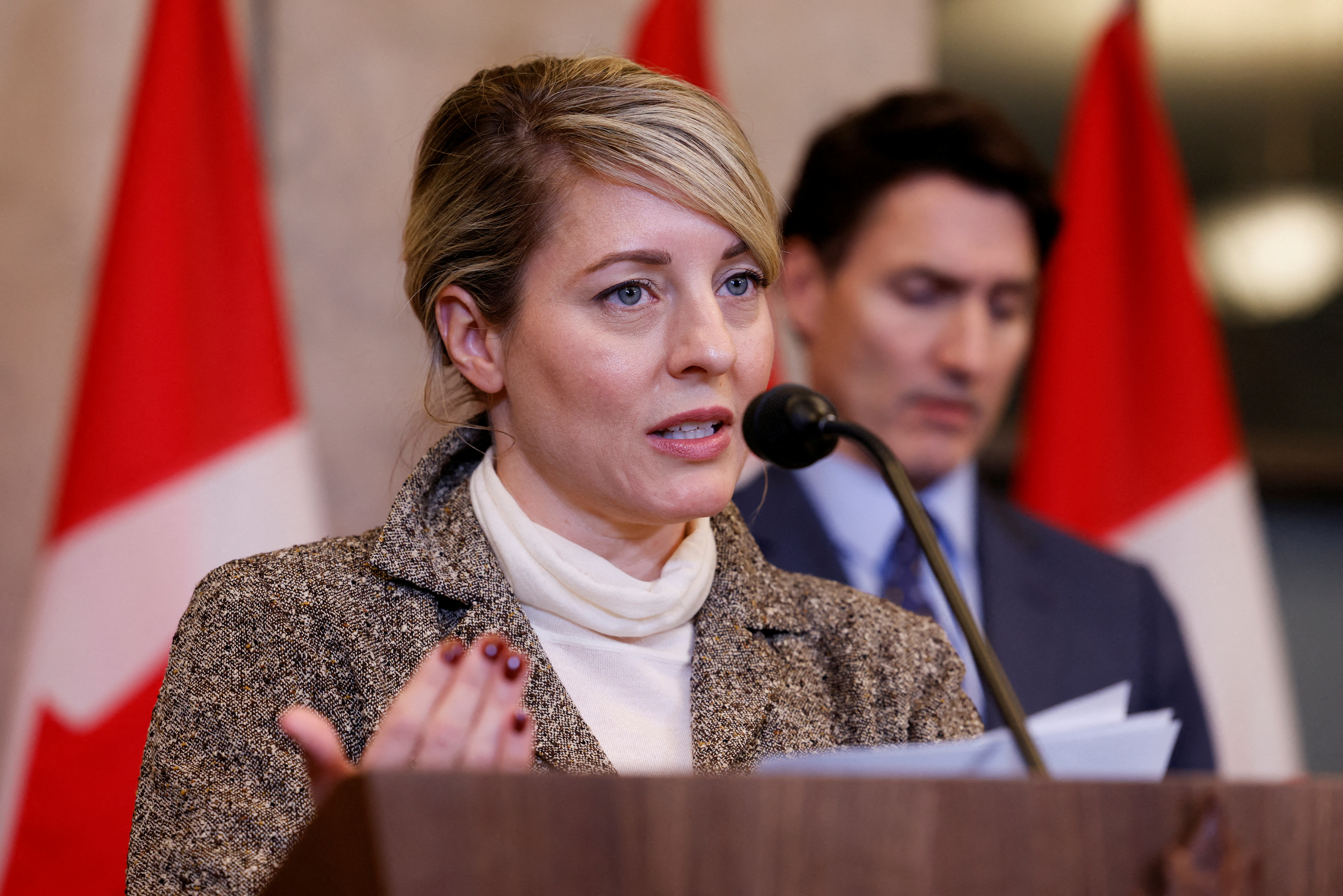 a woman speaks in front of a red and white flag