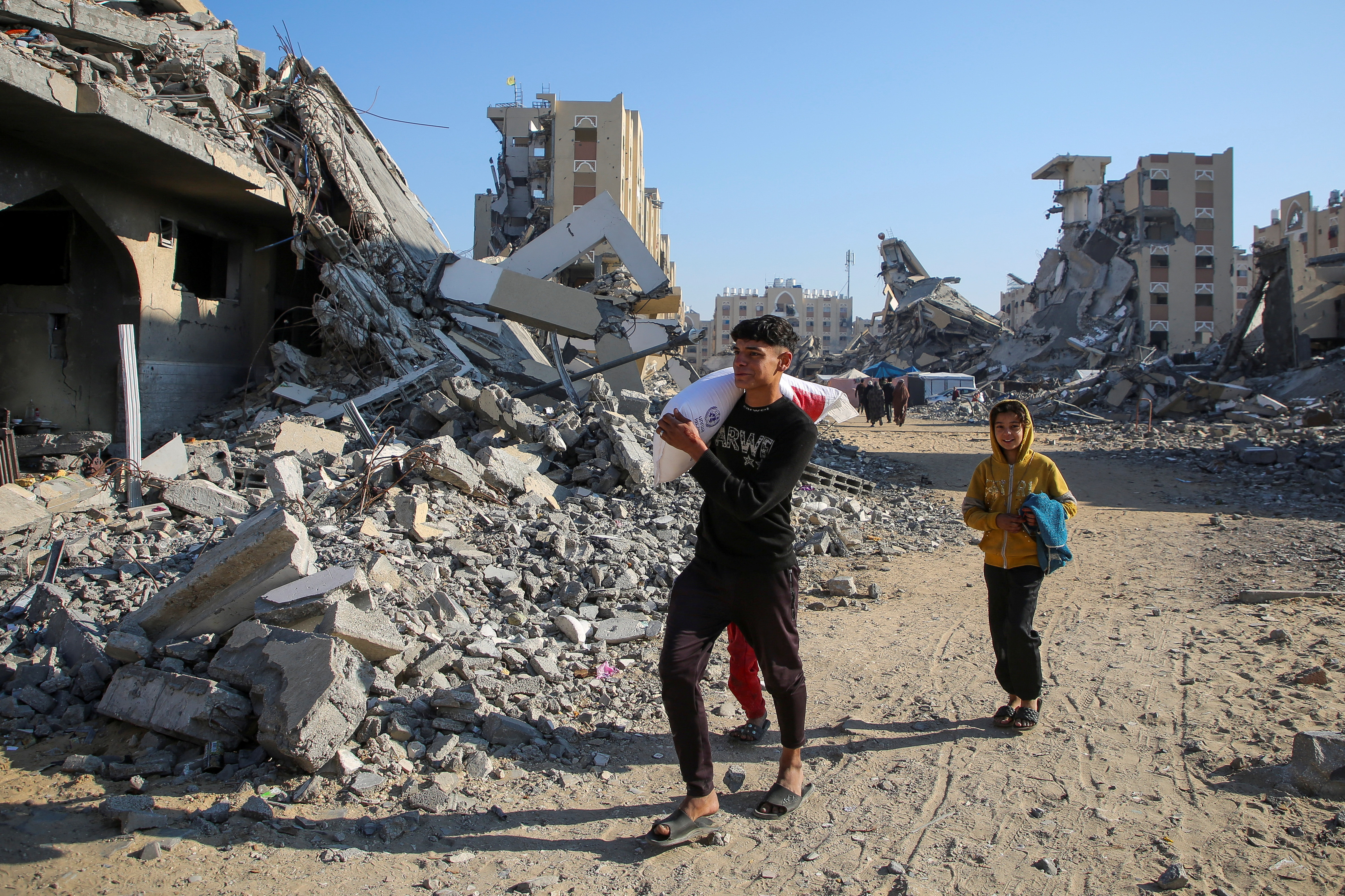 A Palestinian man walks past the rubble as he carries a bag of flour distributed by the United Nation