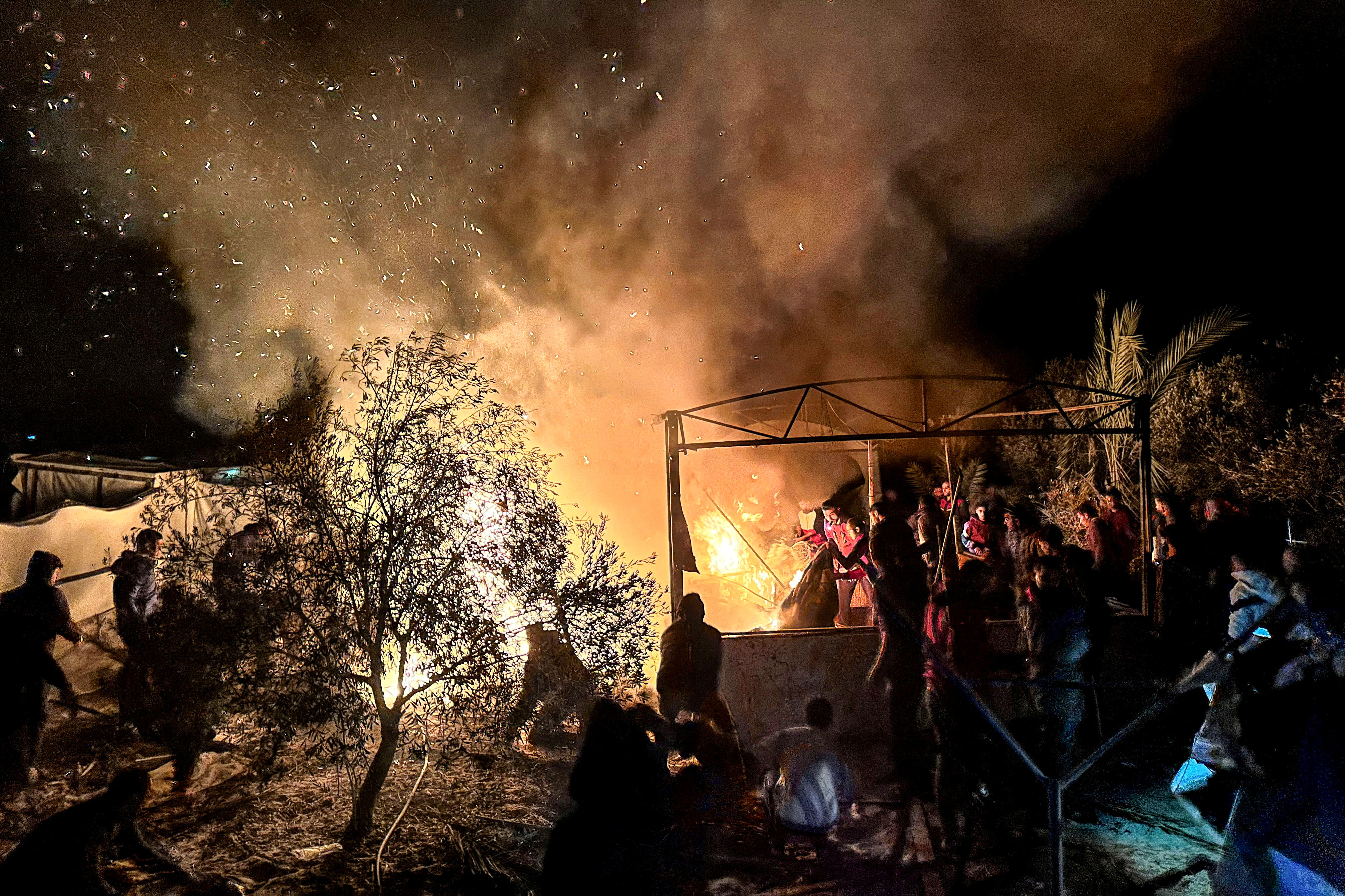 Smoke rises as people stand in a tent camp for displaced people