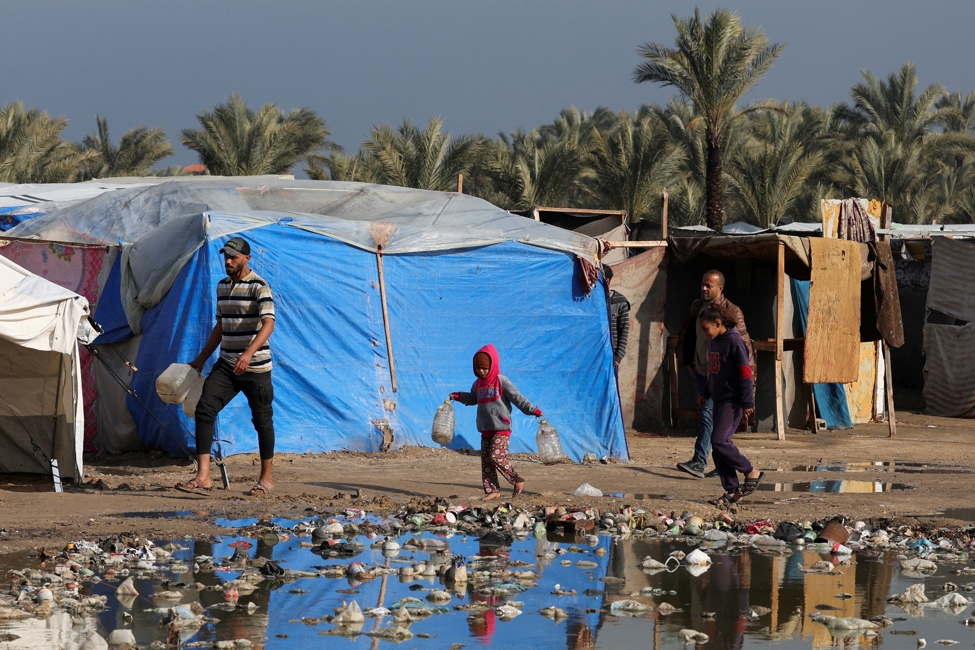Displaced Palestinians walk at a tent camp where they shelter, following heavy rains, amid the Israel-Hamas conflict, in Deir Al-Balah, in the central Gaza Strip, December 30