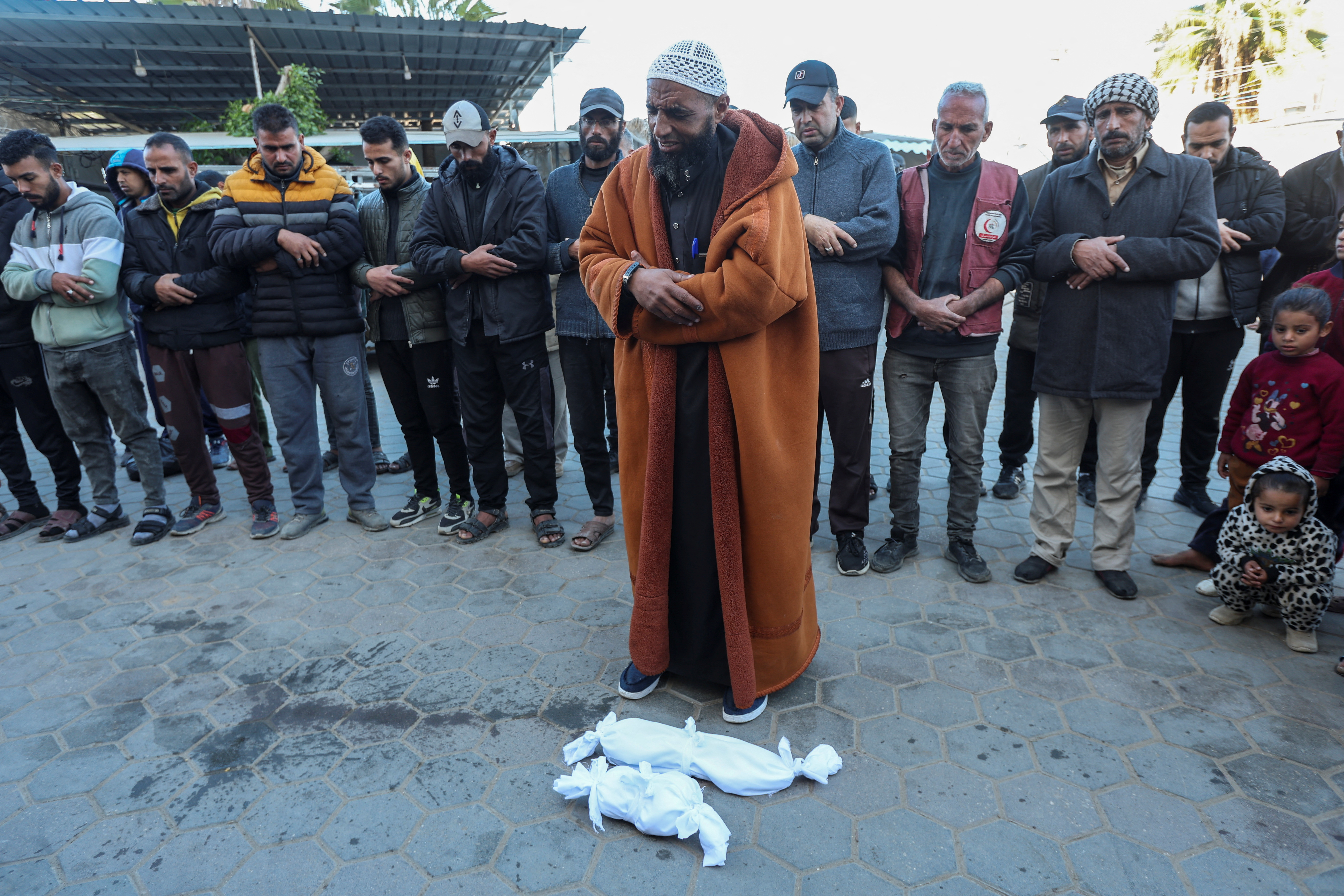 People pray next to the bodies of two Palestinian babies, including infant Jumaa Al-Batran, who died of hypothermia after living in a tent with his displaced family, at Al-Aqsa Martyrs Hospital in Deir Al-Balah in the central Gaza Strip, December 29