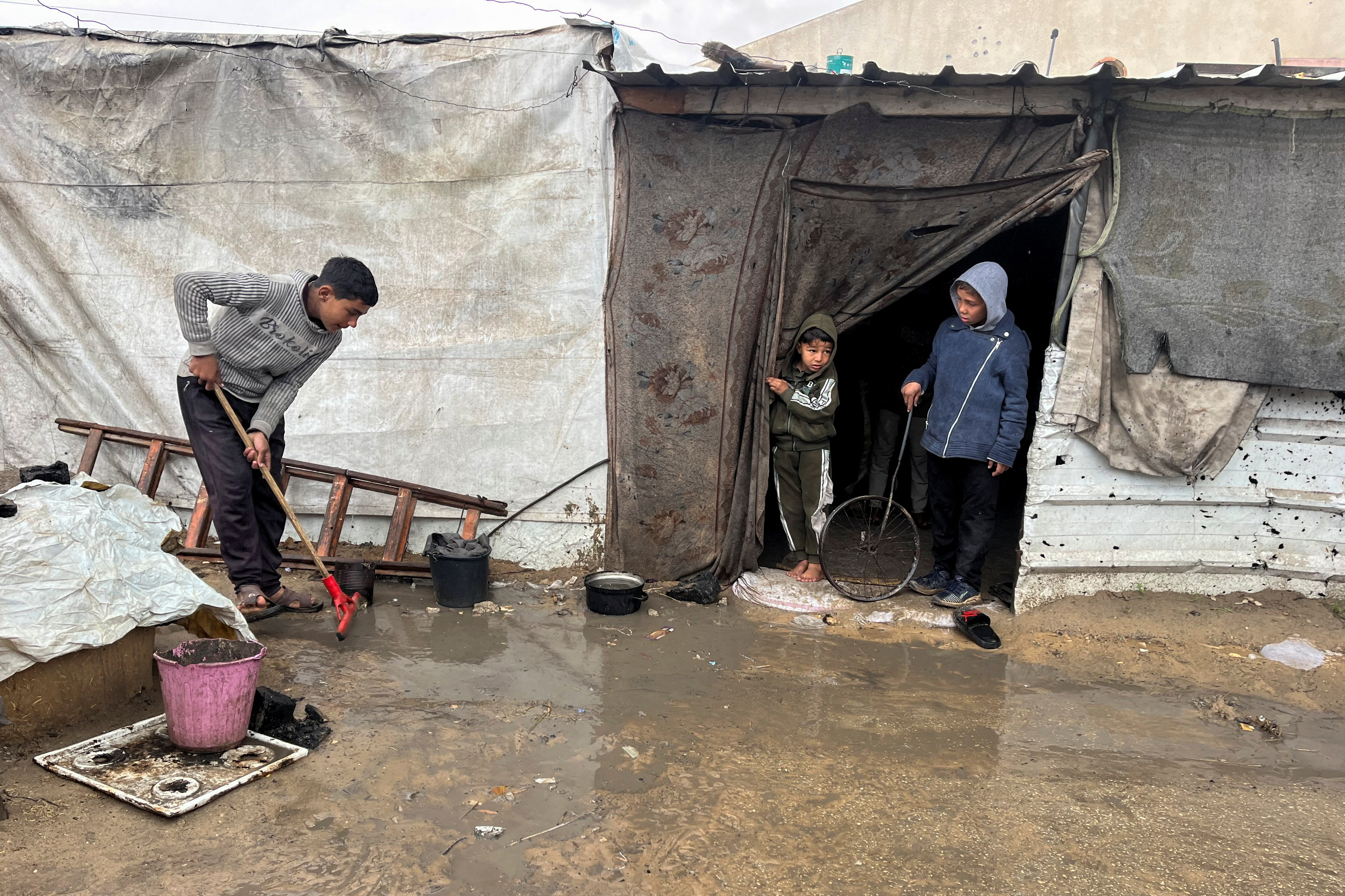 A displaced Palestinian works to remove water and mud at tent camp
