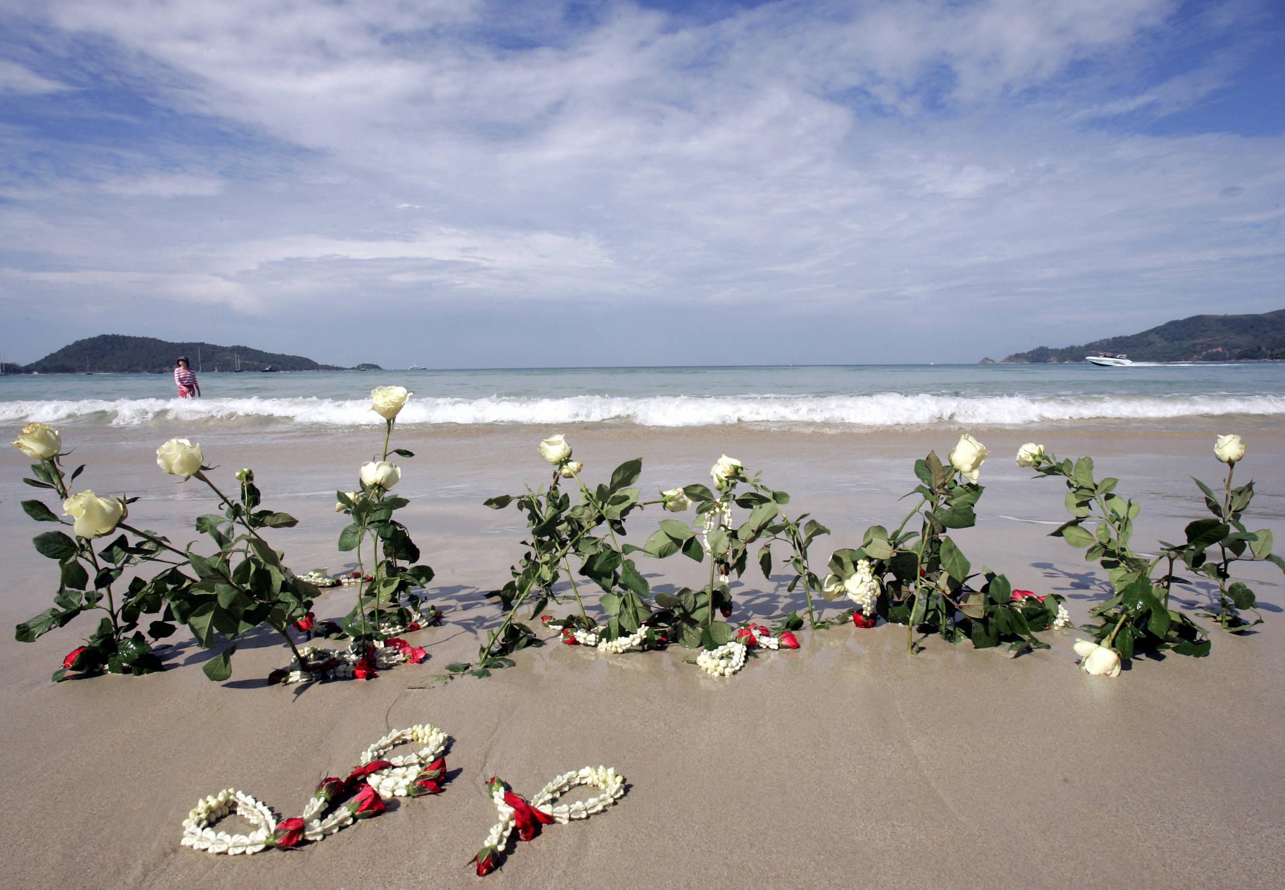Flowers are planted in the sand as survivors and relatives of the 26 December 2004 victims mark the first anniversary of the disaster at Patong beach, in Phuket, southern Thailand, 26 December 2005. Survivors and relatives tossed flowers into the sea and hugged each other to fight off tears as they gathered in this Thai resort to remember their loved ones killed in the tsunami a year ago. AFP PHOTO/PORNCHAI KITTIWONGSAKUL (Photo by PORNCHAI KITTIWONGSAKUL / AFP)