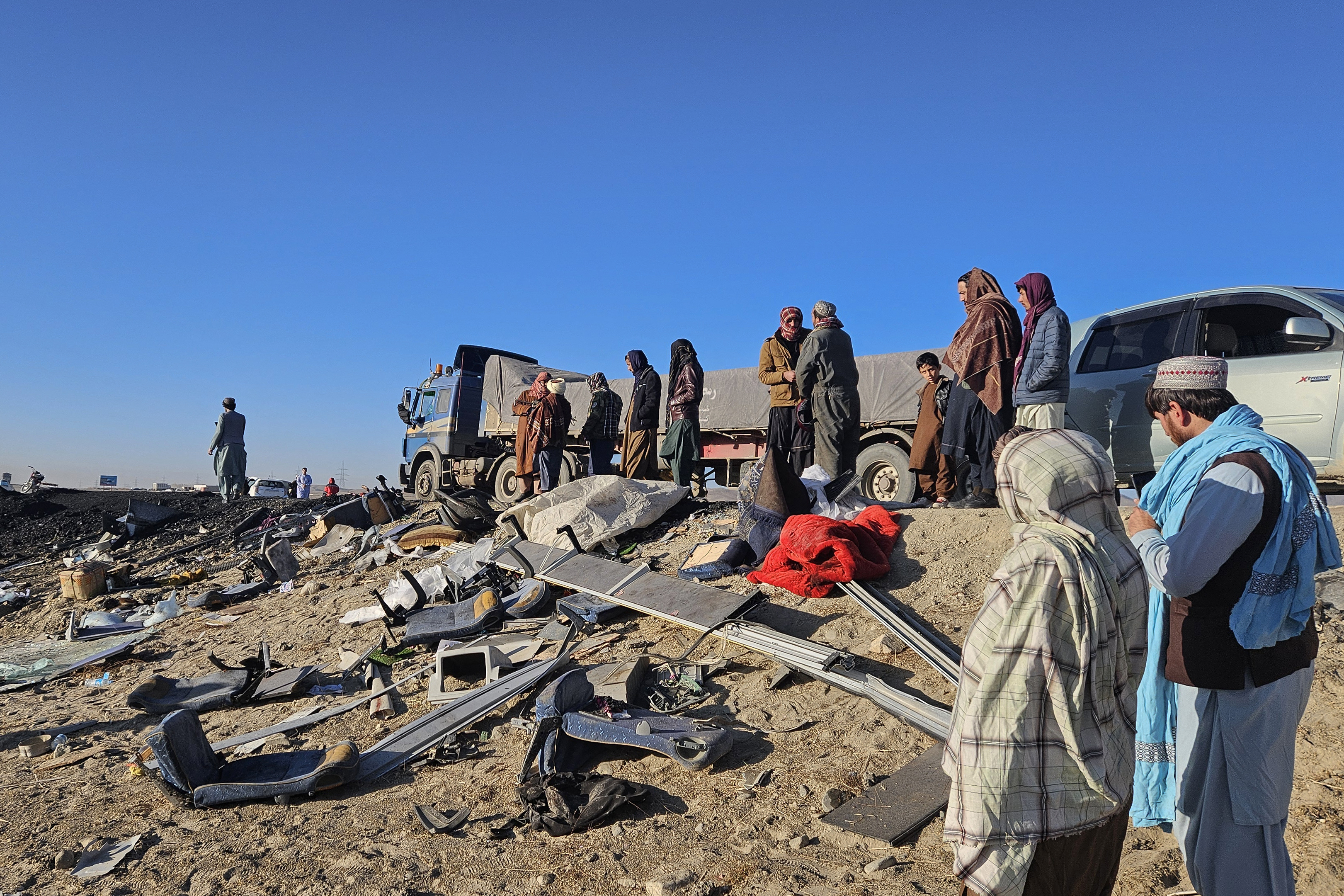 Afghan residents inspect the accident site as they stand near the remains of a bus