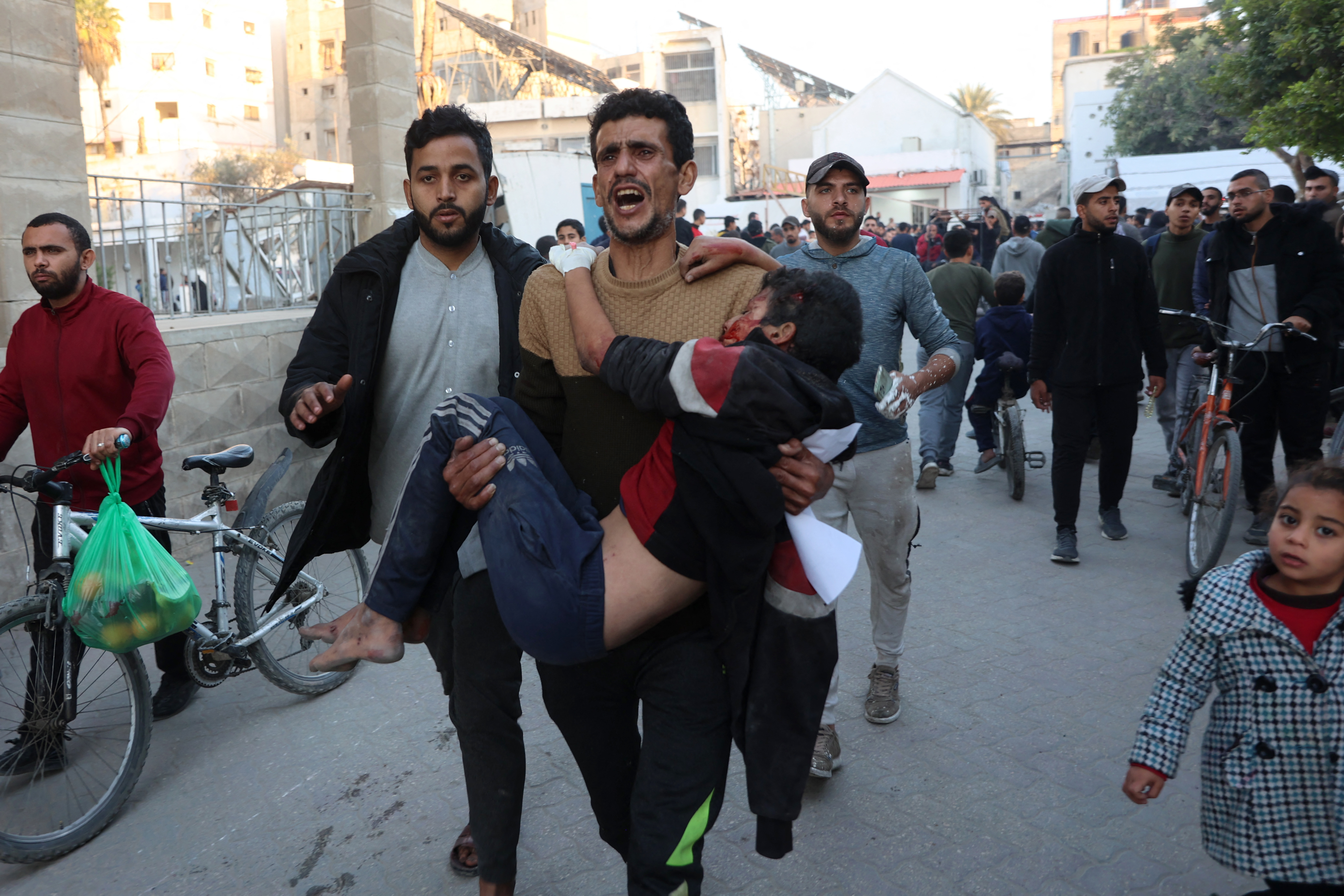 A Palestinian man carries a wounded boy, after an Israeli strike on a school, into the Al-Ahli Arab hospital, also known as the Baptist hospital, in Gaza City on December 19