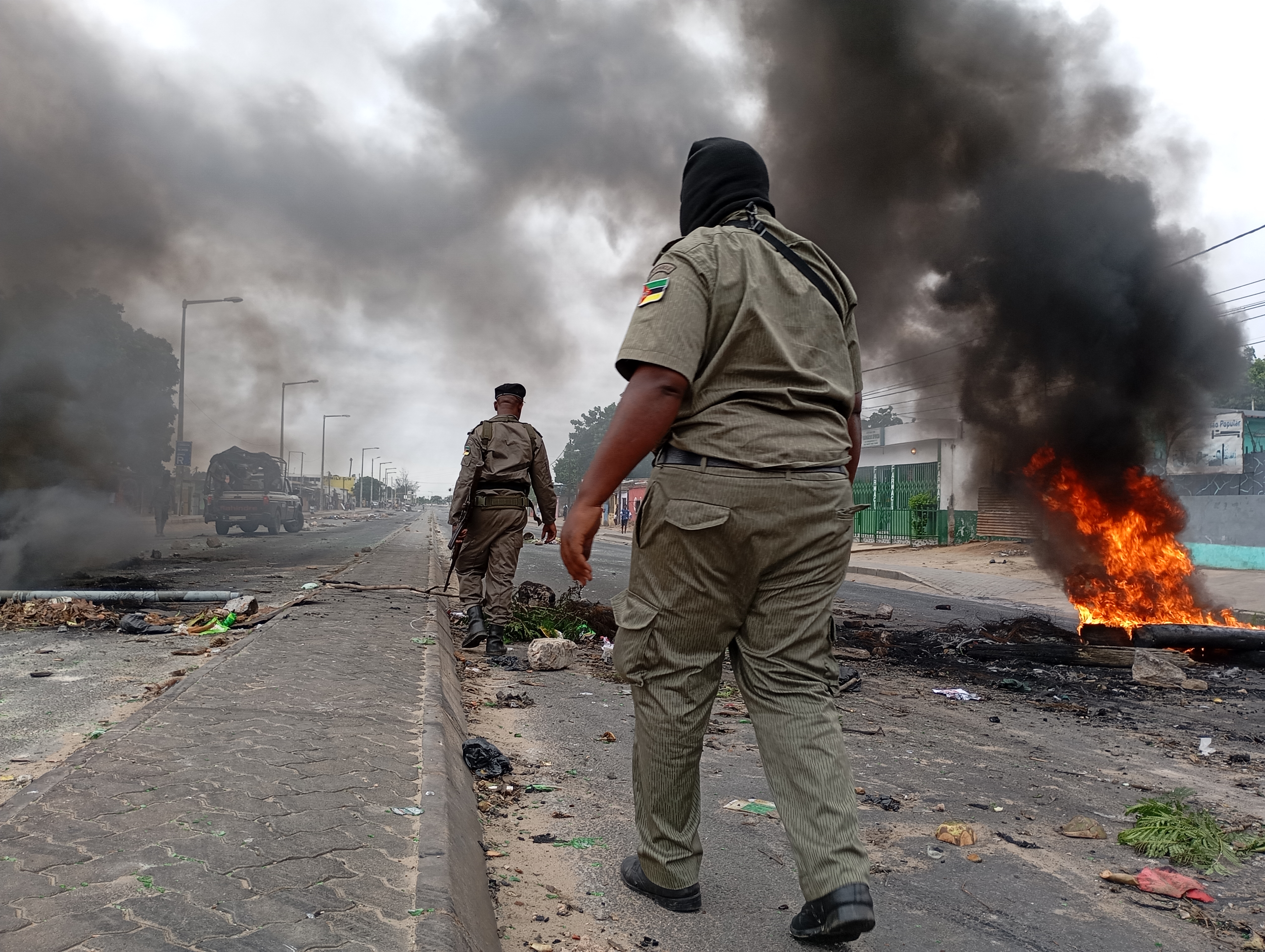 Mozambican security forces are seen next to a burning barricade in Maputo on December 24, 2024. - The capital of Mozambique was deserted on Tuesday, its main arteries heavily secured, noted AFP, the day after the confirmation of the victory in the October elections of Frelimo, in power for half a century, while the opposition maintains his denunciations of fraud. Maputo remains frozen in a climate of fear and insecurity on Christmas Eve after violent demonstrations in the evening and night. The police, in armored vehicles, patrol the center. (Photo by Amilton Neves / AFP)