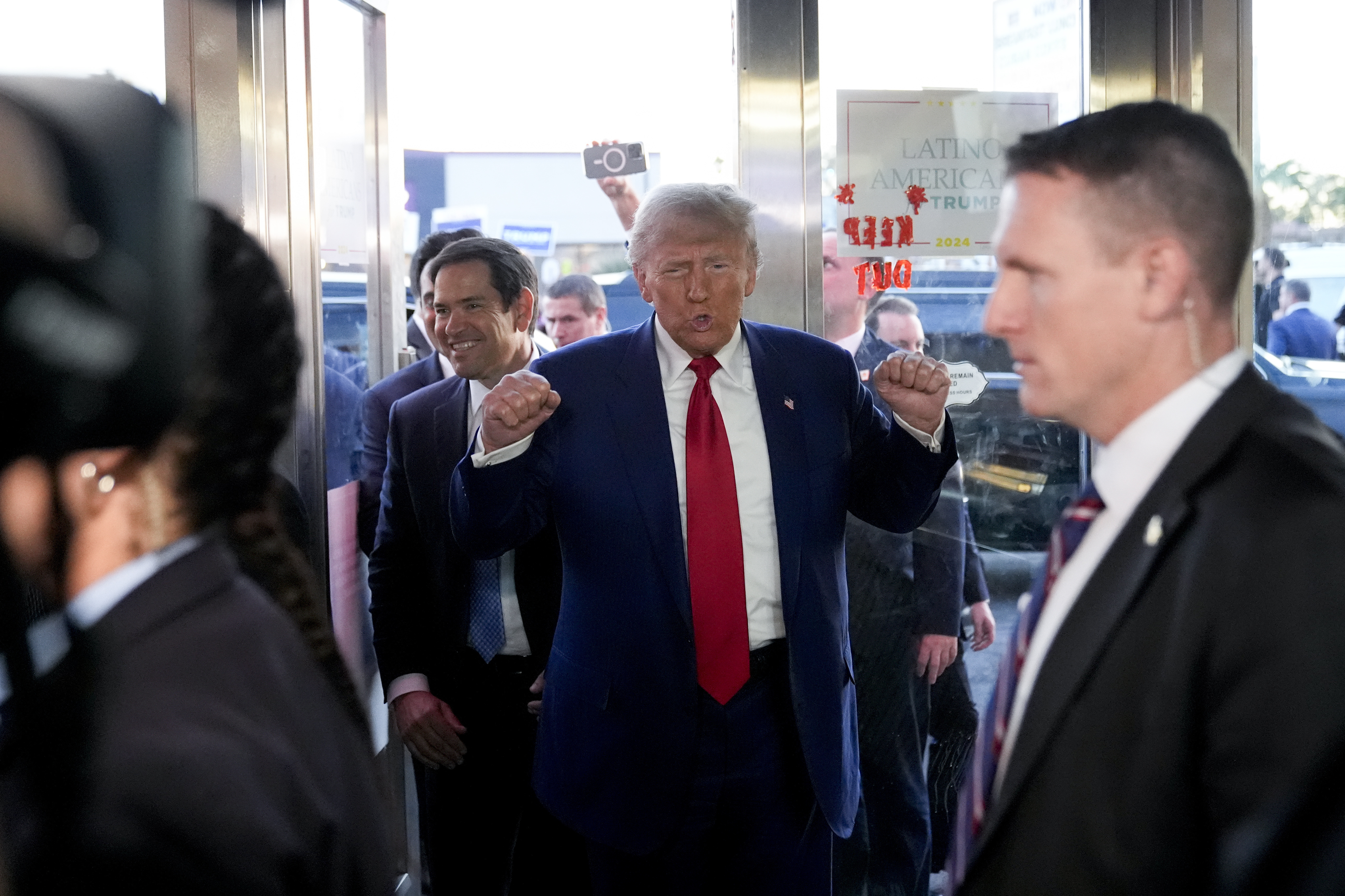 Donald Trump arrives at a Cuban cafe, raising two fists for the camera and surrounded by his entourage