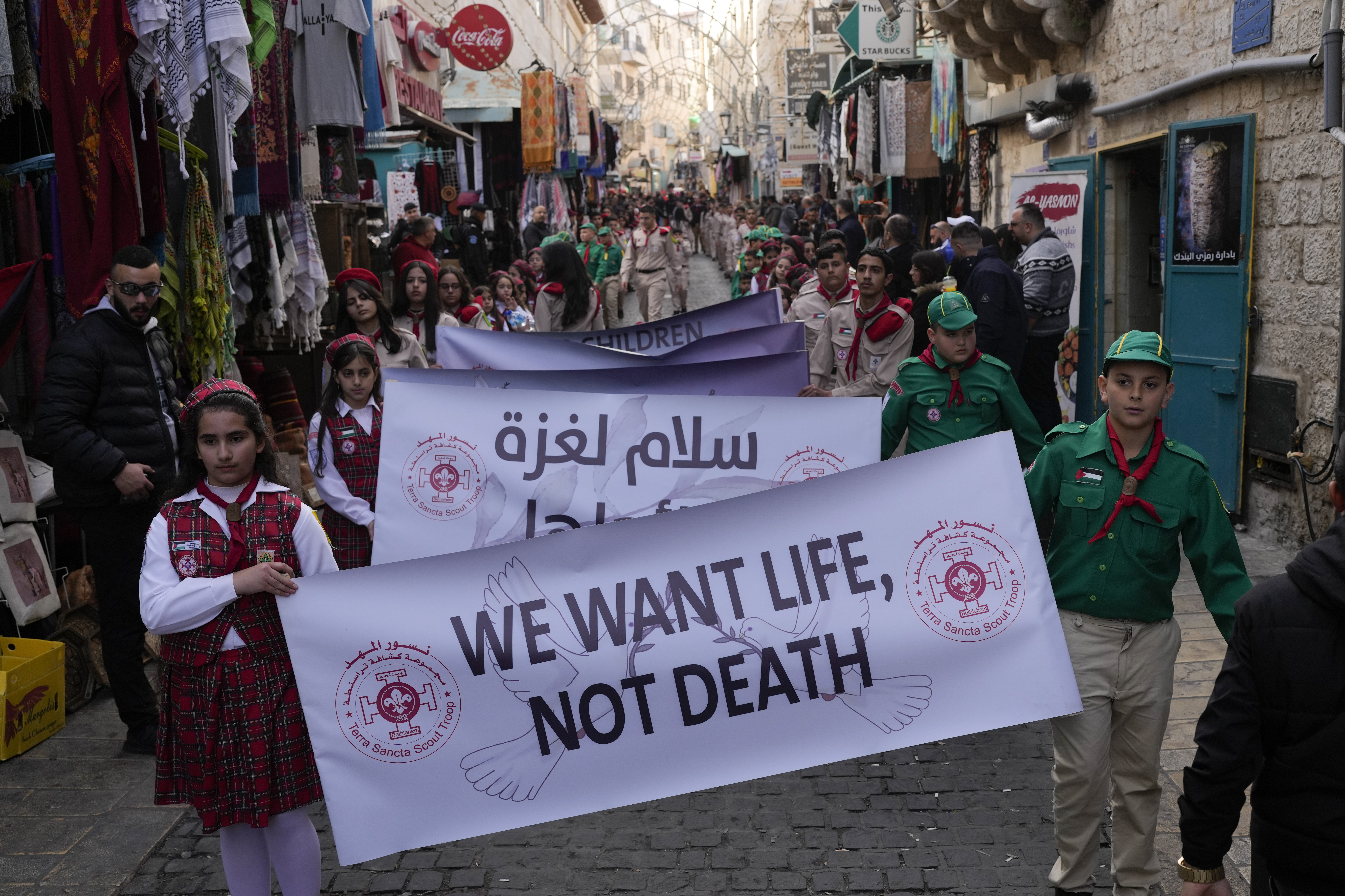 Scouts hold a sign that reads "We want life, not death" during the traditional Christian procession towards the Church of the Nativity, traditionally believed to be the birthplace of Jesus, on Christmas Eve, in the West Bank city of Bethlehem, Tuesday, Dec. 24