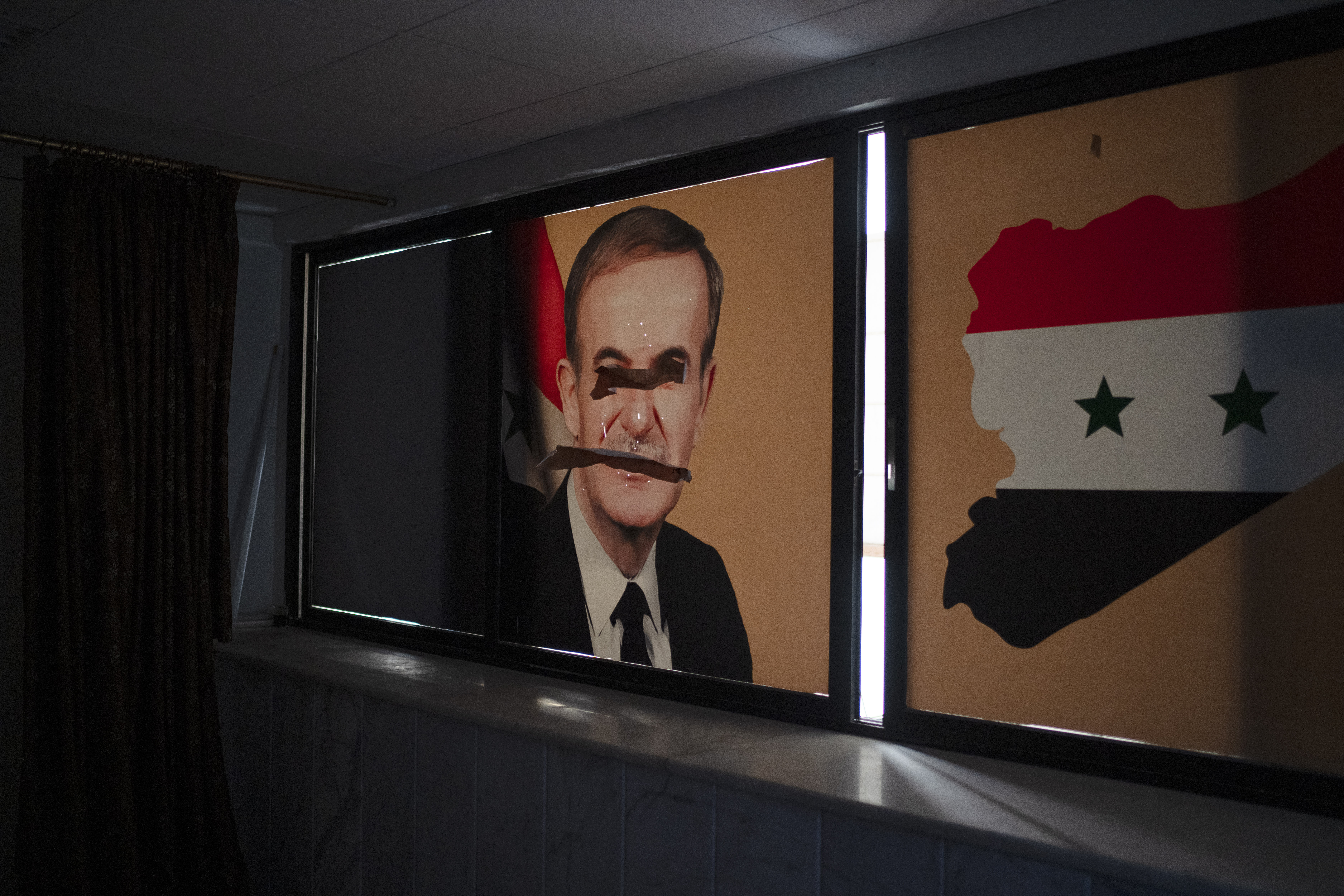 A damaged image depicting the late Syrian President Hafez al-Assad, is seen on a window of the Police headquarters in Homs, Syria, Thursday, Dec. 26