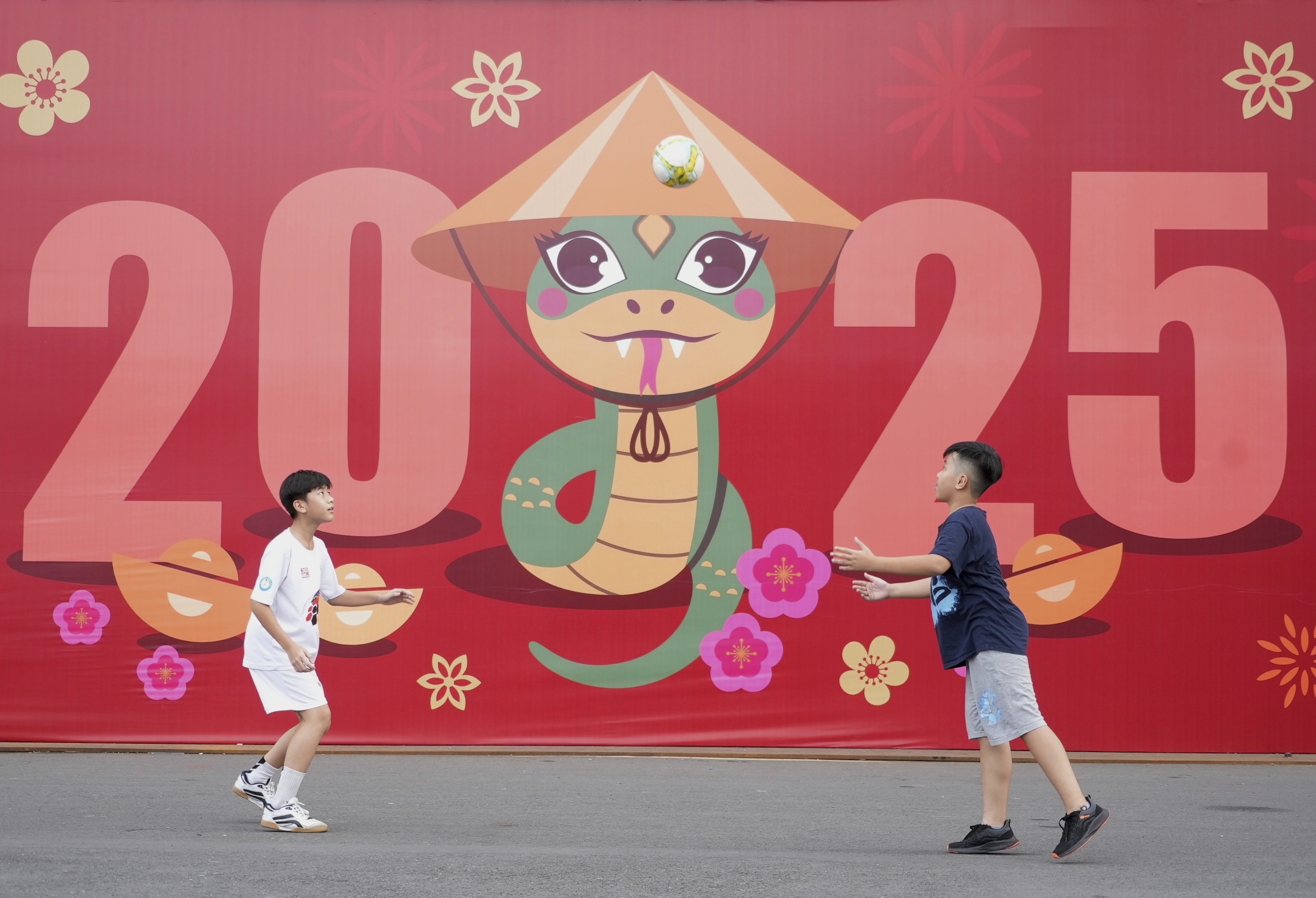 Two boys play football in front of a billboard welcoming the New Year 2025 in Ho Chi Minh city, Vietnam on Tuesday, Dec.31